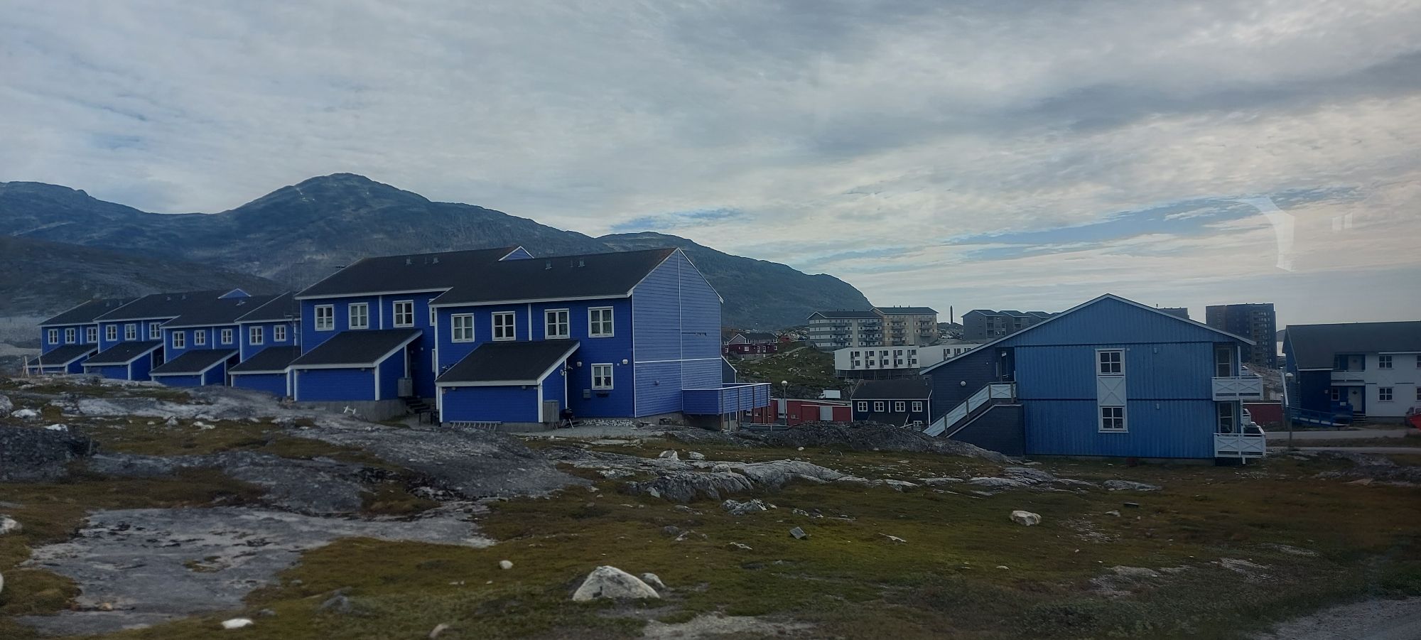 Aerial view of Greenlandic settlement with blue and red houses scattered across rocky terrain near fjord