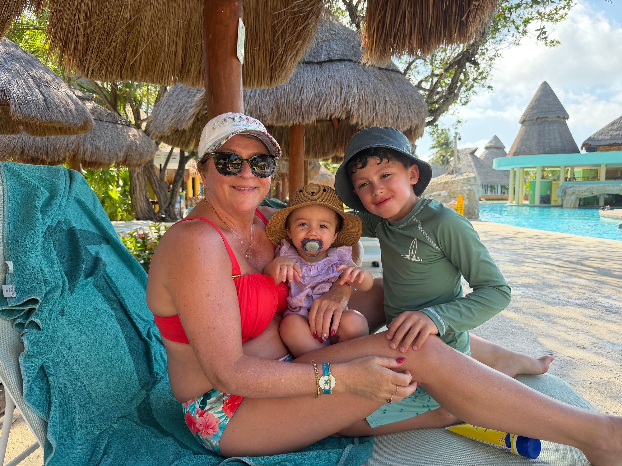 Woman with two children and toddler posing under thatched umbrellas by a resort pool in Playa del Carmen
