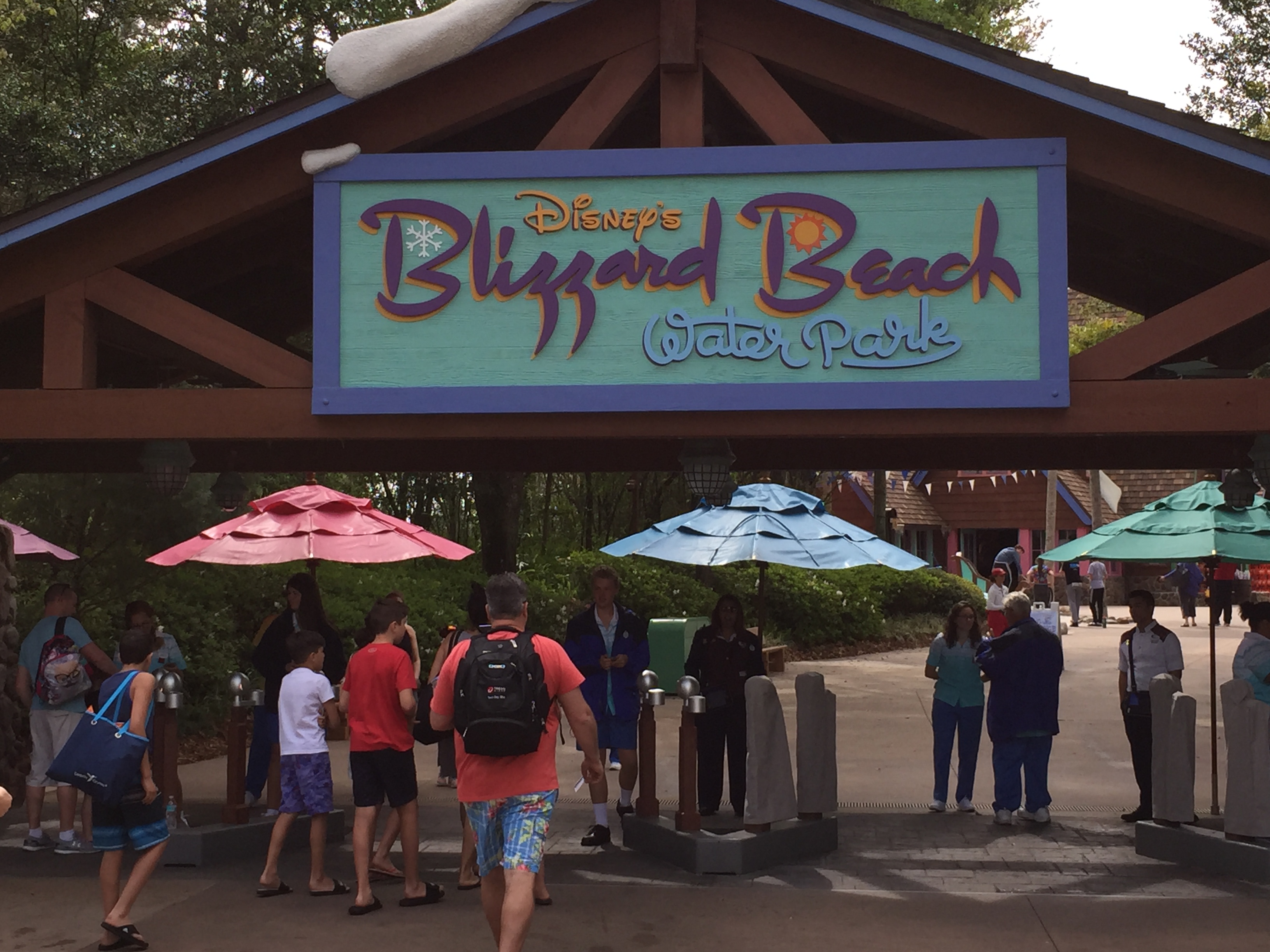 Entrance sign for Disney's Blizzard Beach Water Park with guests gathered under umbrellas on a sunny day