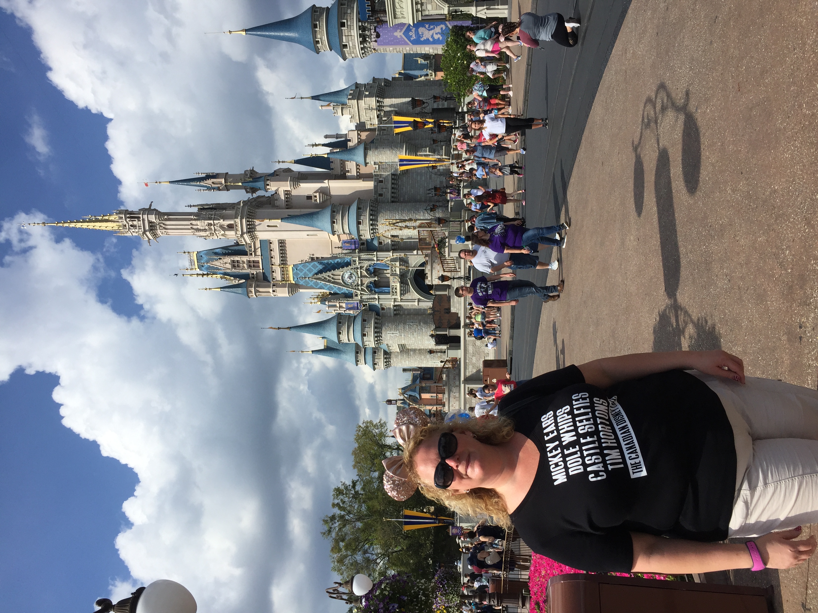 MaryBeth posing in front of Cinderella Castle in daylight wearing Mickey-themed apparel and sunglasses
