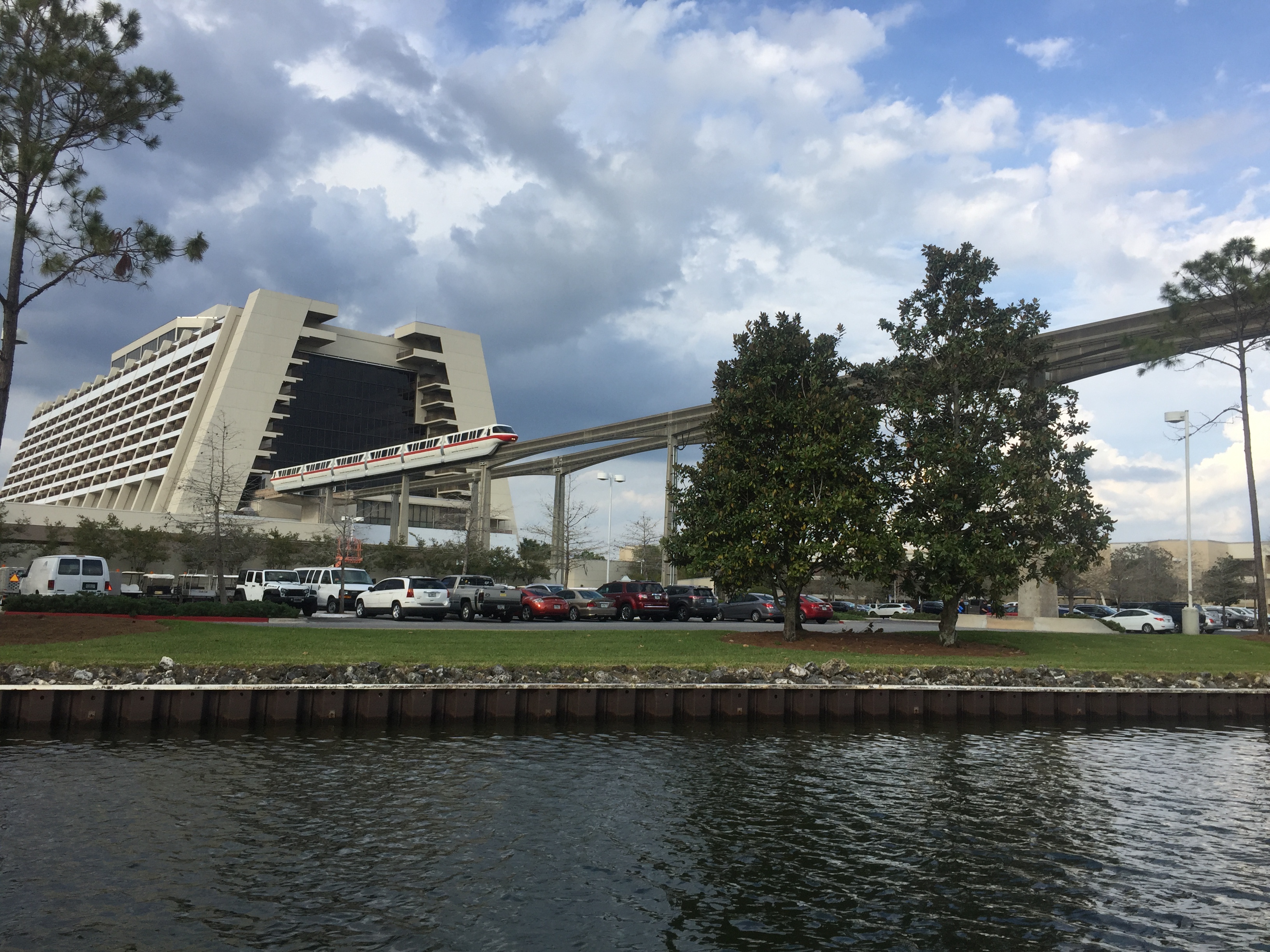 Monorail train crossing over a modern hotel building beside a waterway on a partly cloudy day