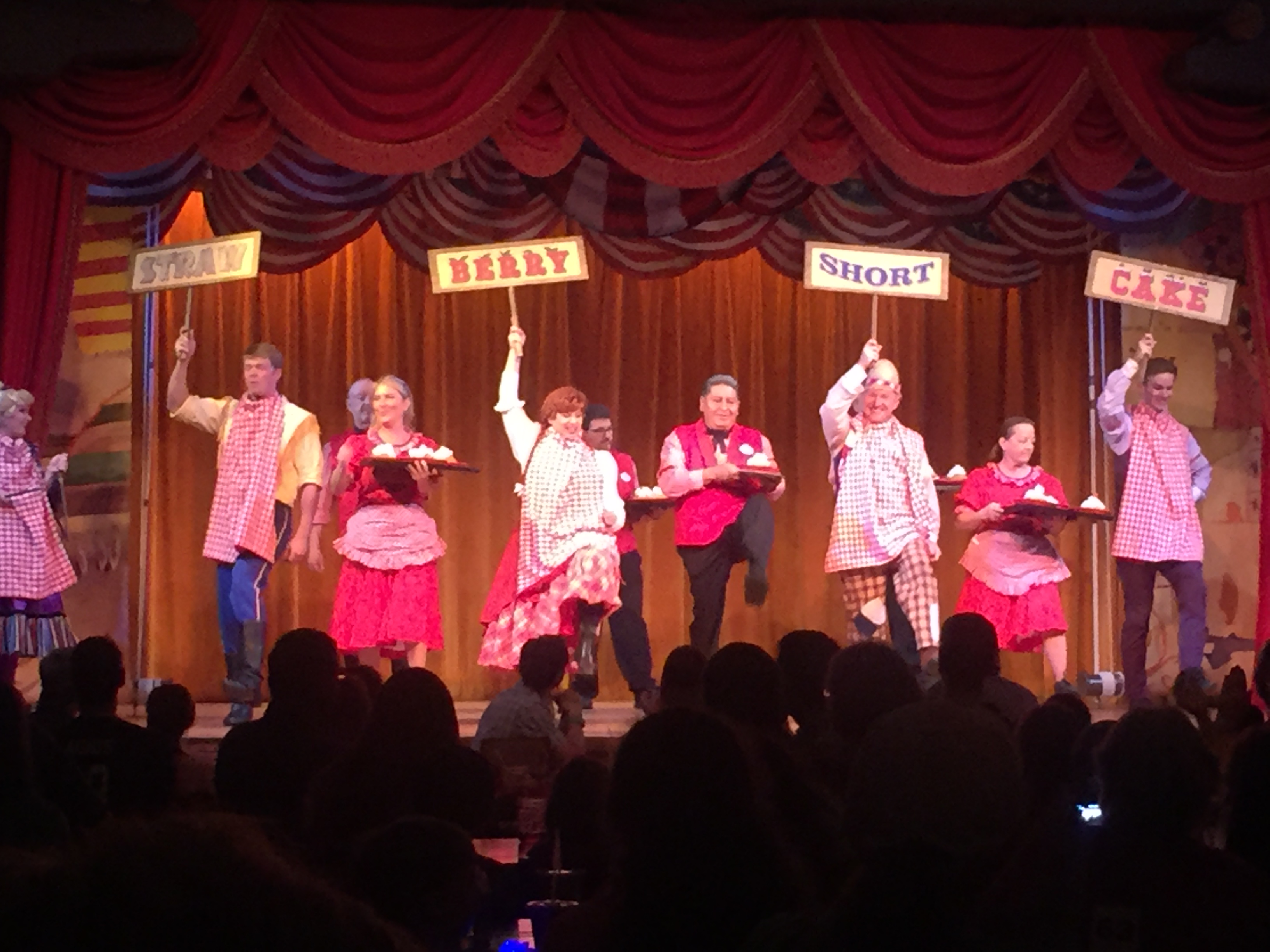 Performers on stage in pink and red costumes during a musical theater show with dramatic lighting