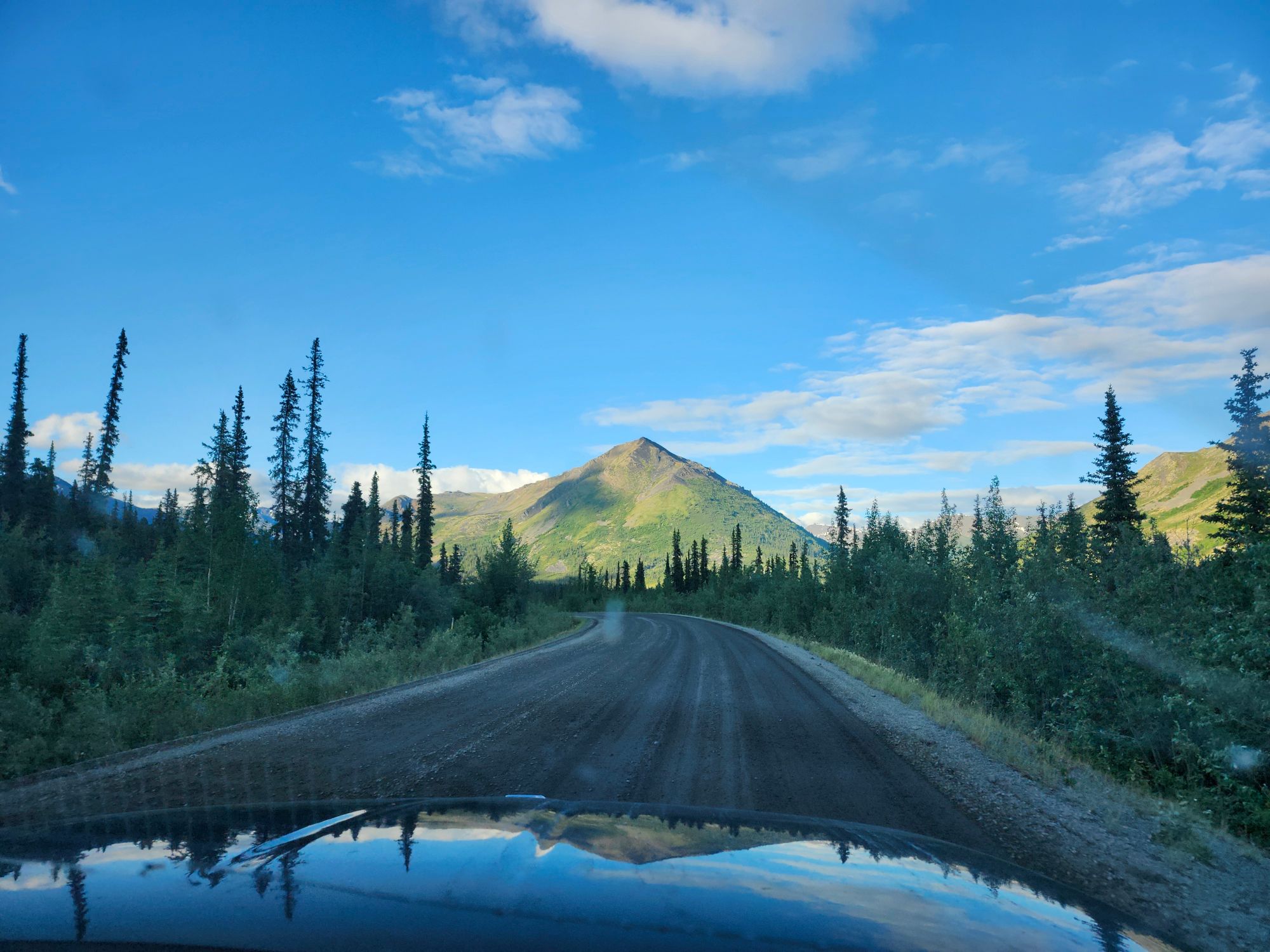 Gravel road stretching toward a cone-shaped mountain through sparse northern forest