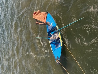 A woman in an orange life jacket sits in a blue kayak on the Nile River