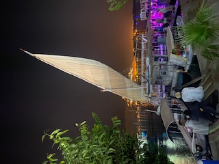 A traditional Egyptian felucca sailboat with white sail is illuminated at night along the Nile