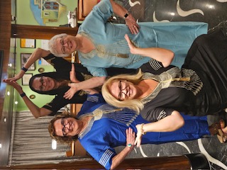 Four women pose together indoors, smiling at the camera in casual travel attire