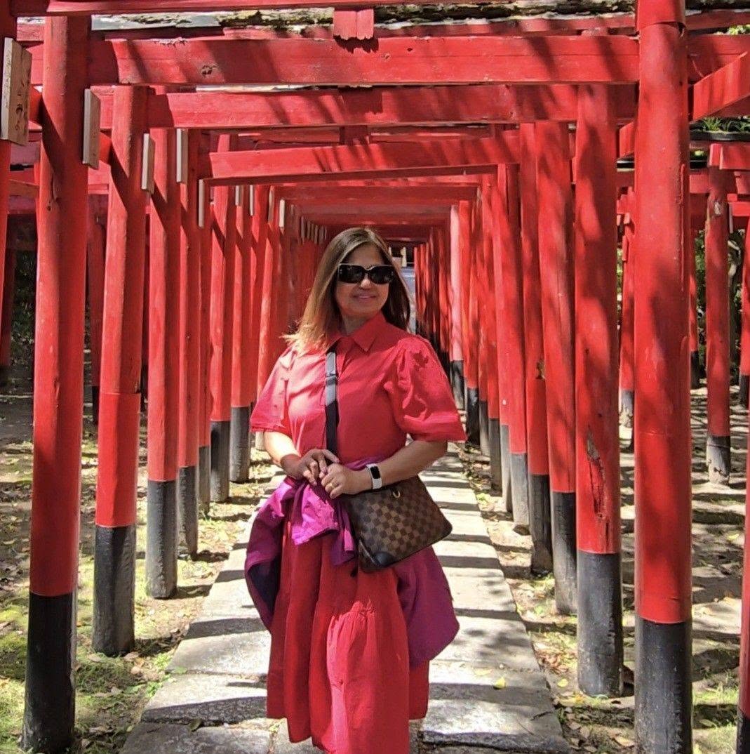 Woman in red shirt walking through tunnel of bright red torii gates at Japanese shrine