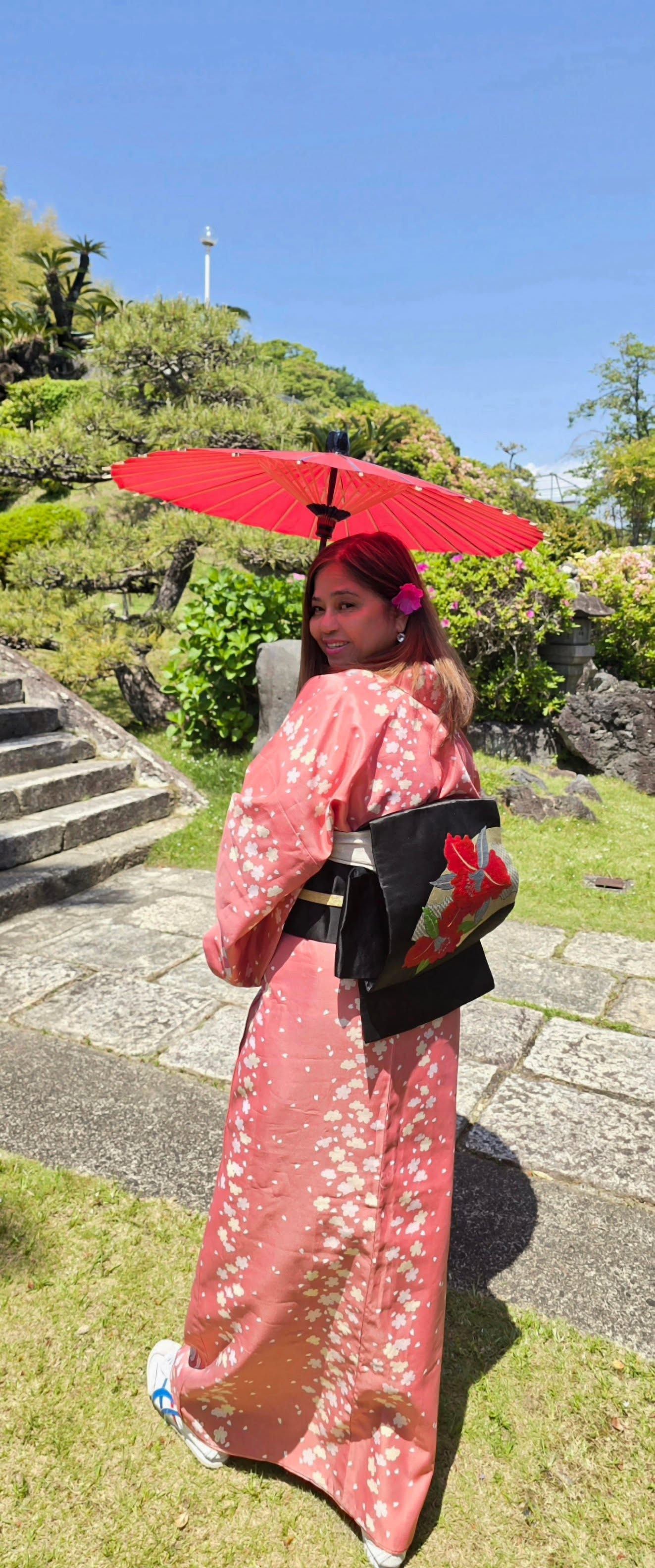 Woman in pink floral yukata holding red parasol at Japanese temple garden with stone lantern
