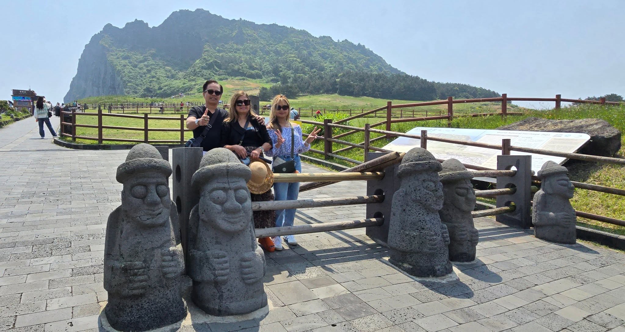 Three people posing with stone statues at Jeju Island volcanic landscape with mountain backdrop
