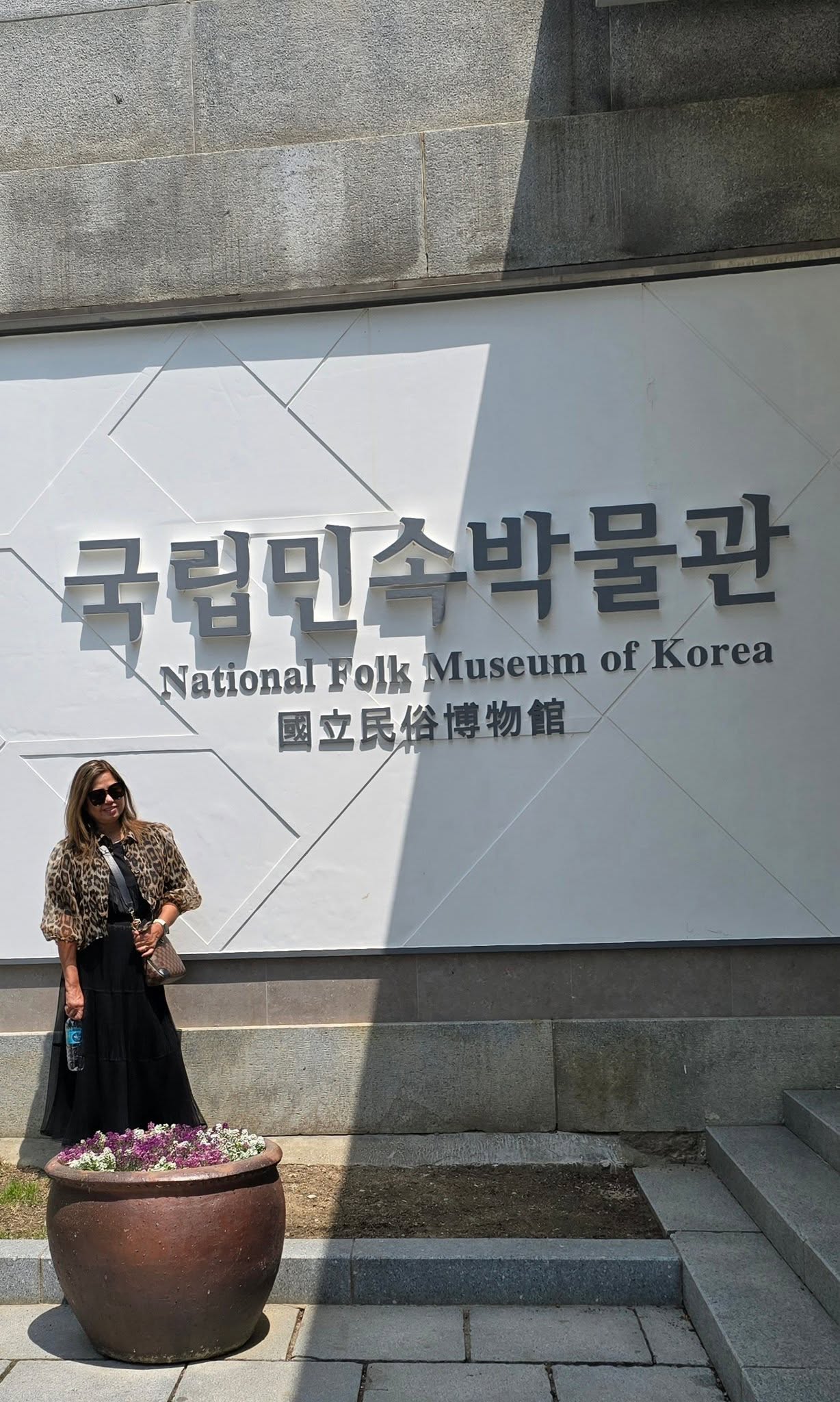 Woman in leopard print jacket at National Folk Museum of Korea entrance sign in Seoul