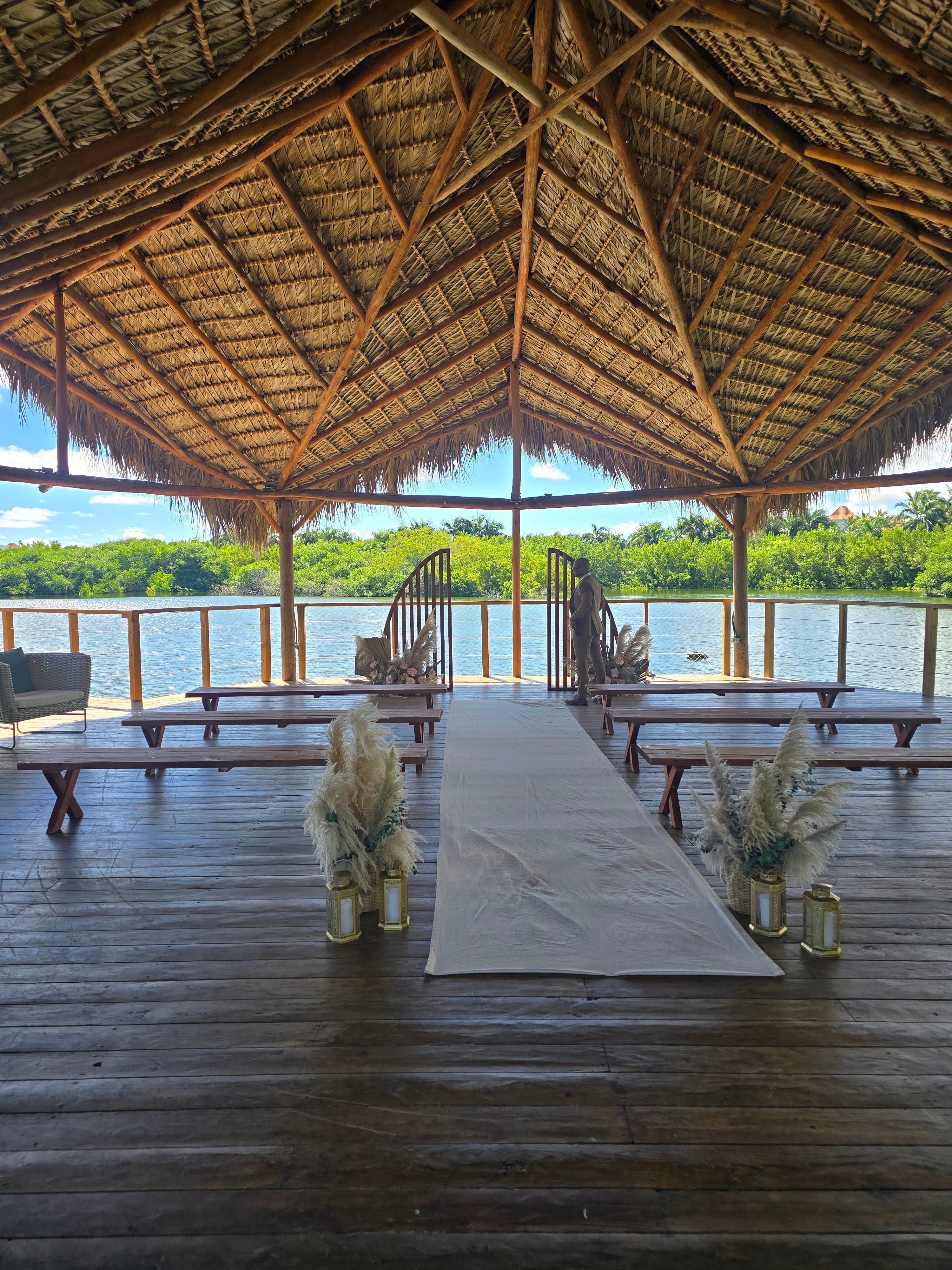 Wooden deck ceremony space with thatched roof shelter overlooking a calm river lined with mangrove trees