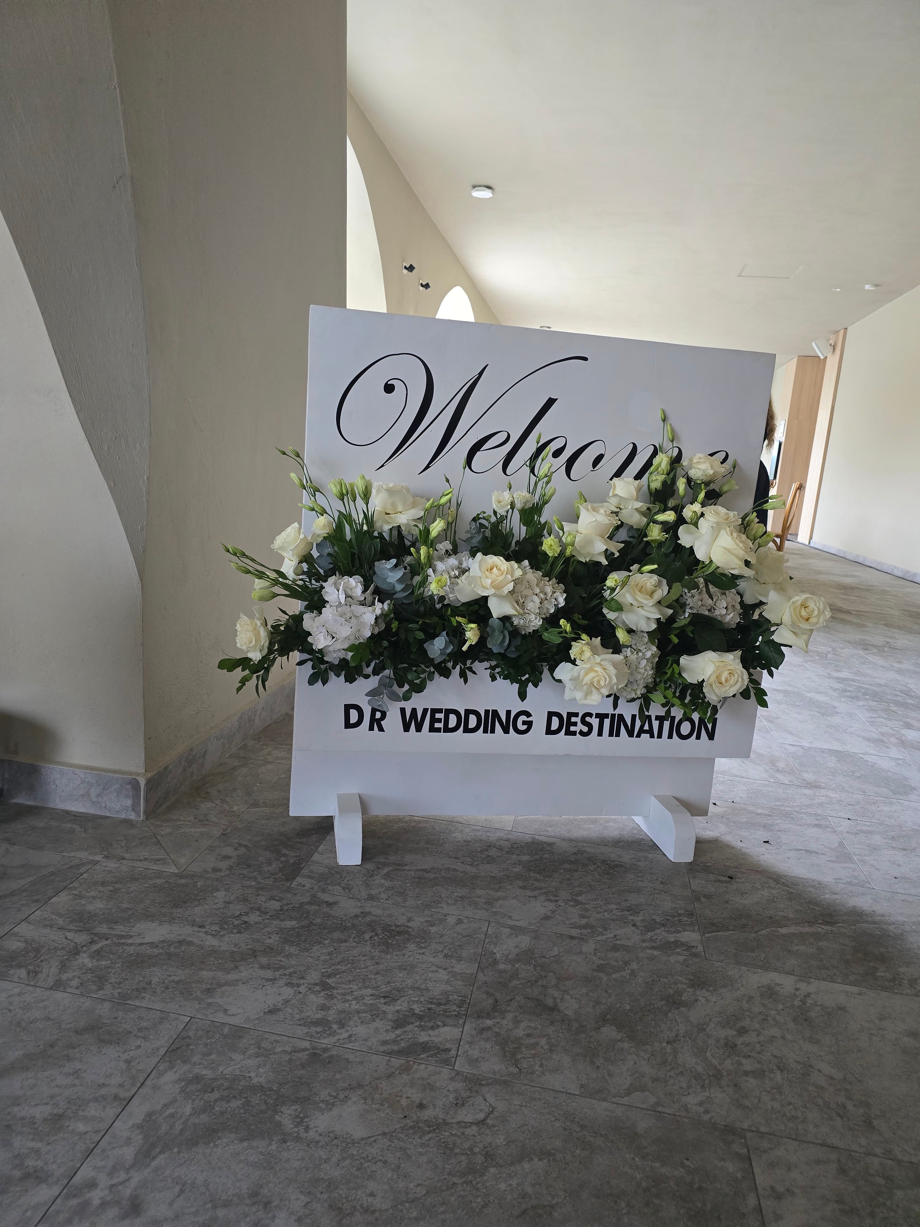 Welcome sign for DR Wedding Destination decorated with white and cream flowers in an indoor venue space