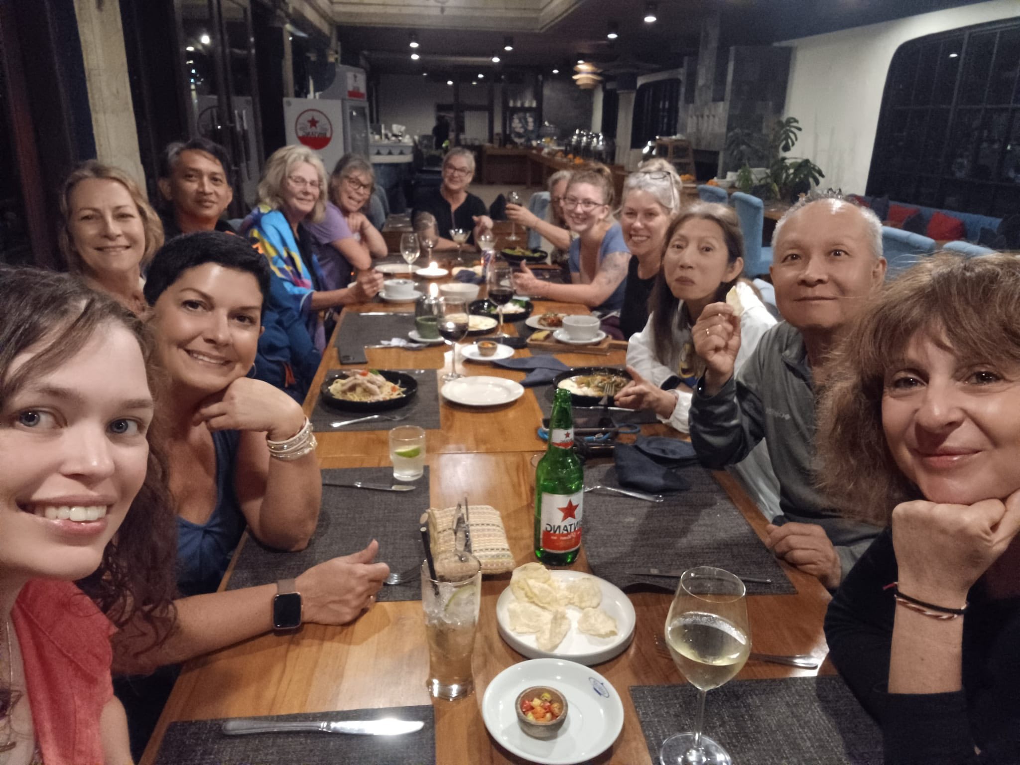 Large group dining together at a long wooden table indoors with food and beverages