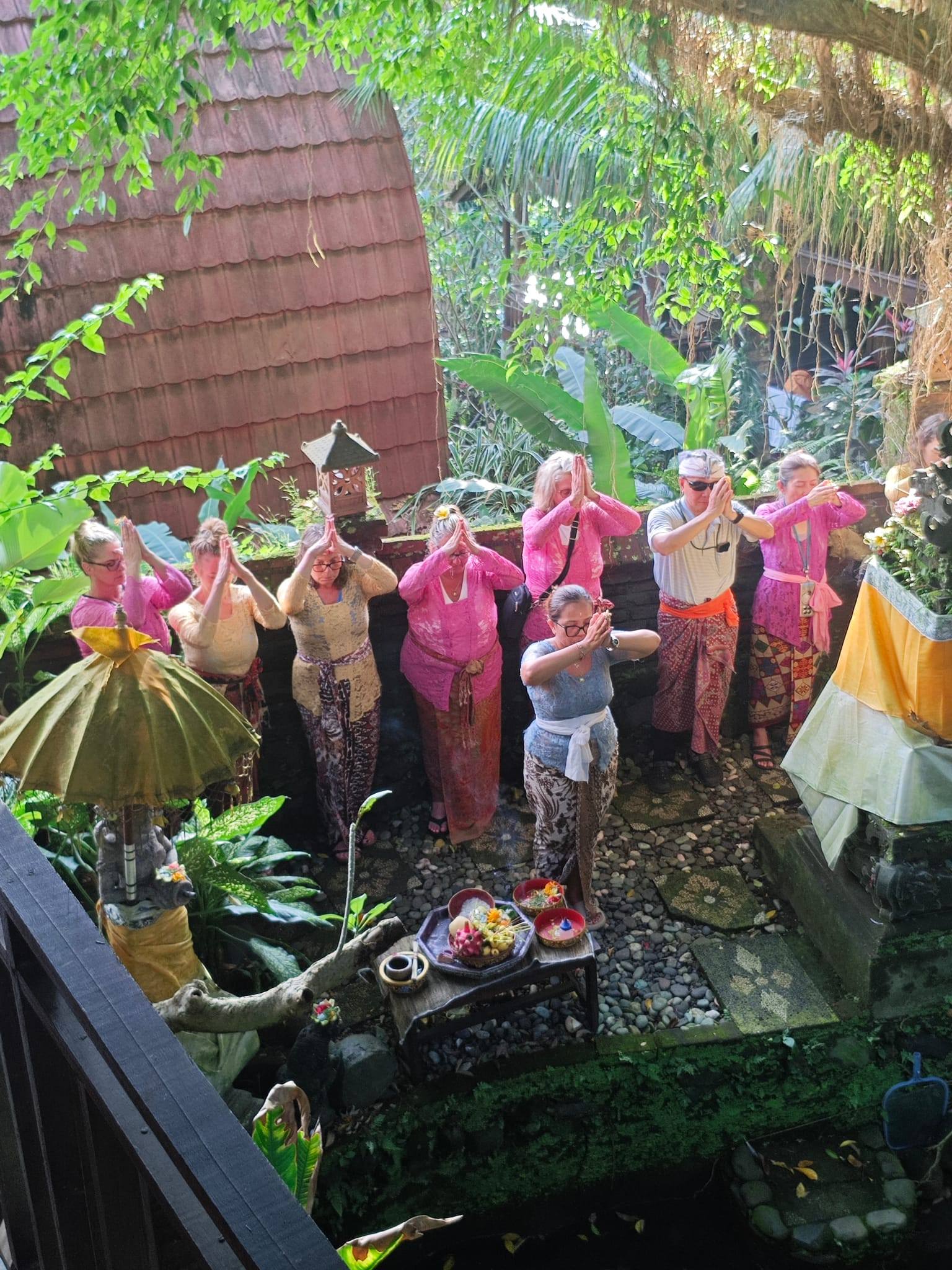 Women in traditional pink and colorful Balinese clothing performing a dance or ceremony in a garden courtyard