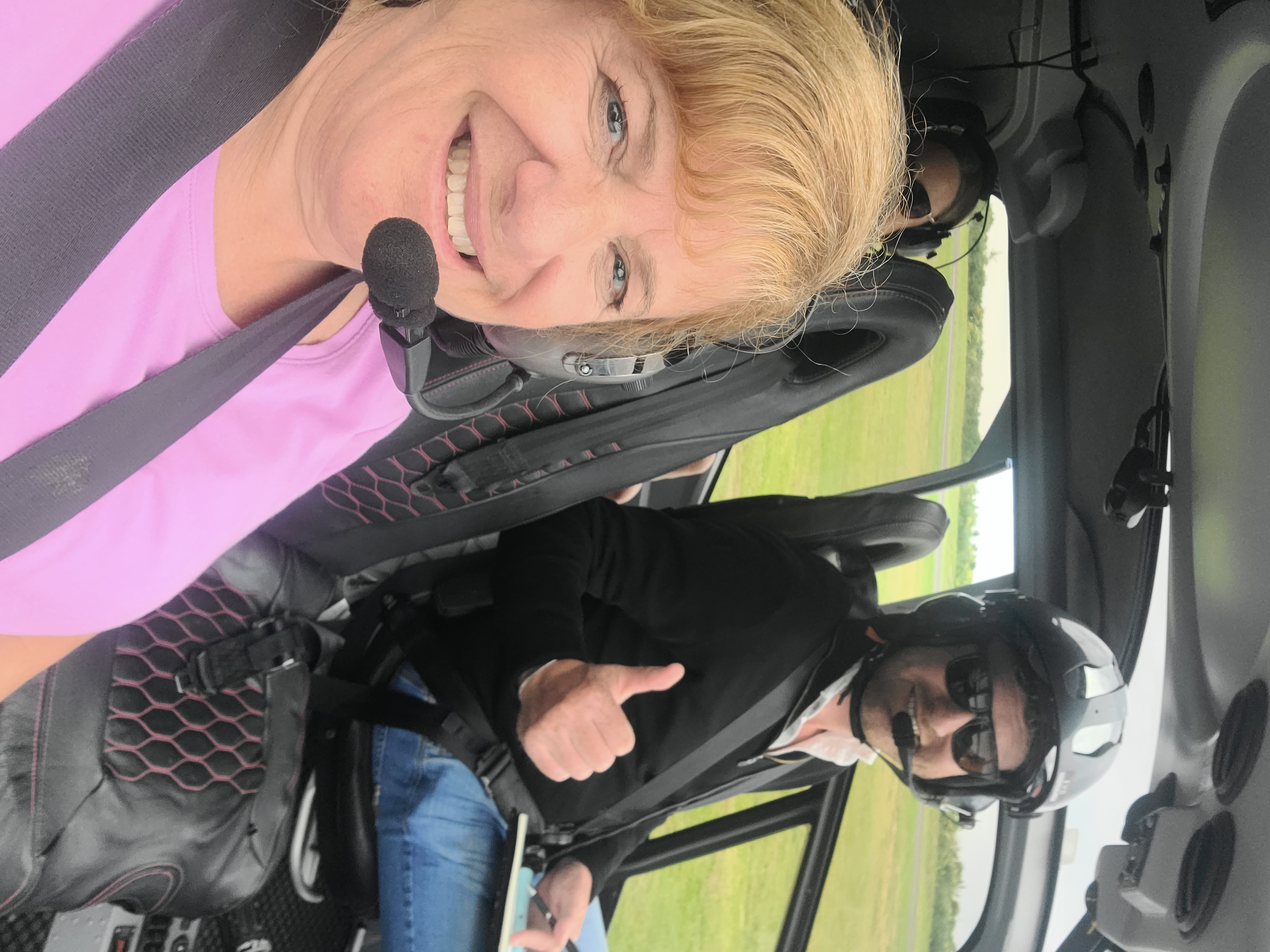 Deborah in a small aircraft with headset, smiling during a scenic flight over New Zealand landscape