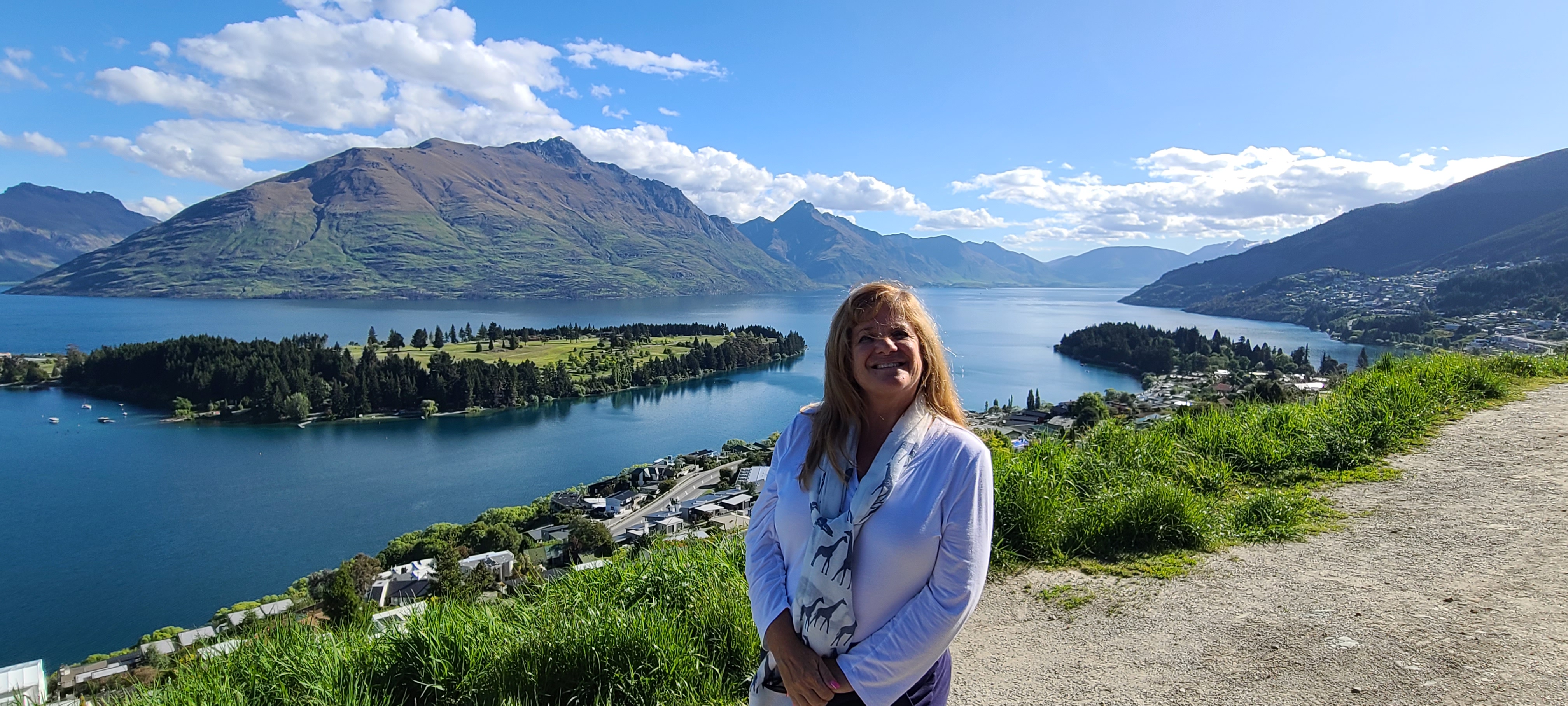Deborah smiling on a balcony overlooking a lake with mountains and forested shores in New Zealand