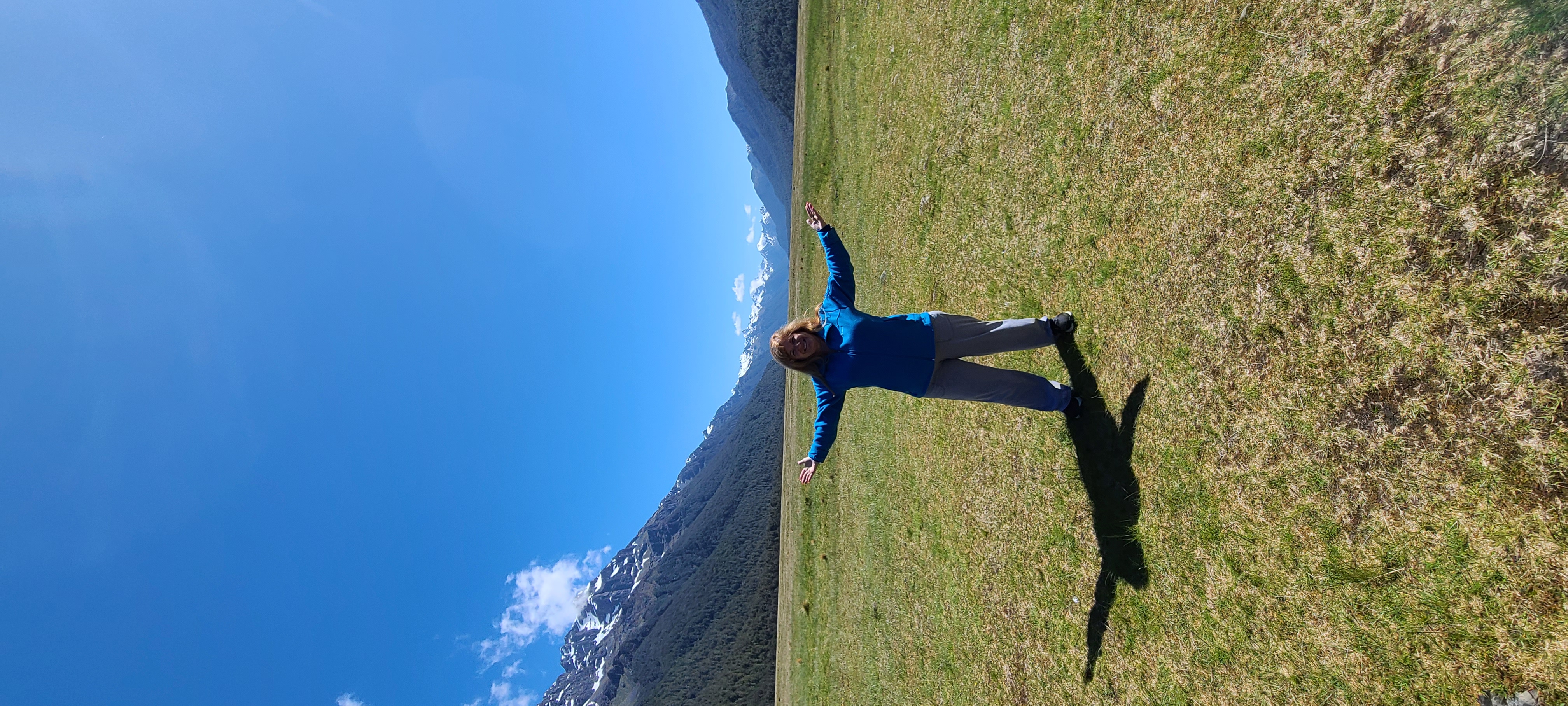 Deborah standing in a vast meadow with snow-capped mountains in the distance, arms outstretched