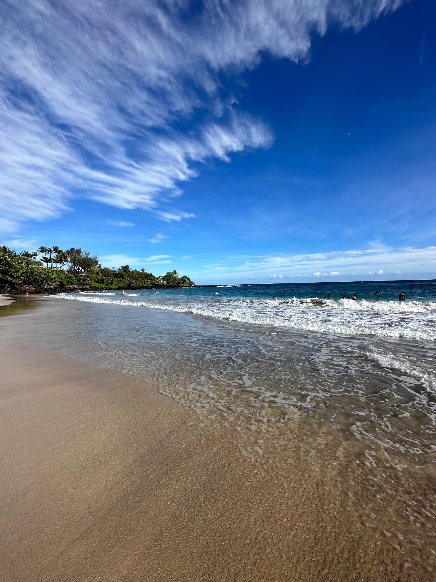 A dramatic rainbow stretches from mountains across a coastal Hawaiian town with lush green valleys visible