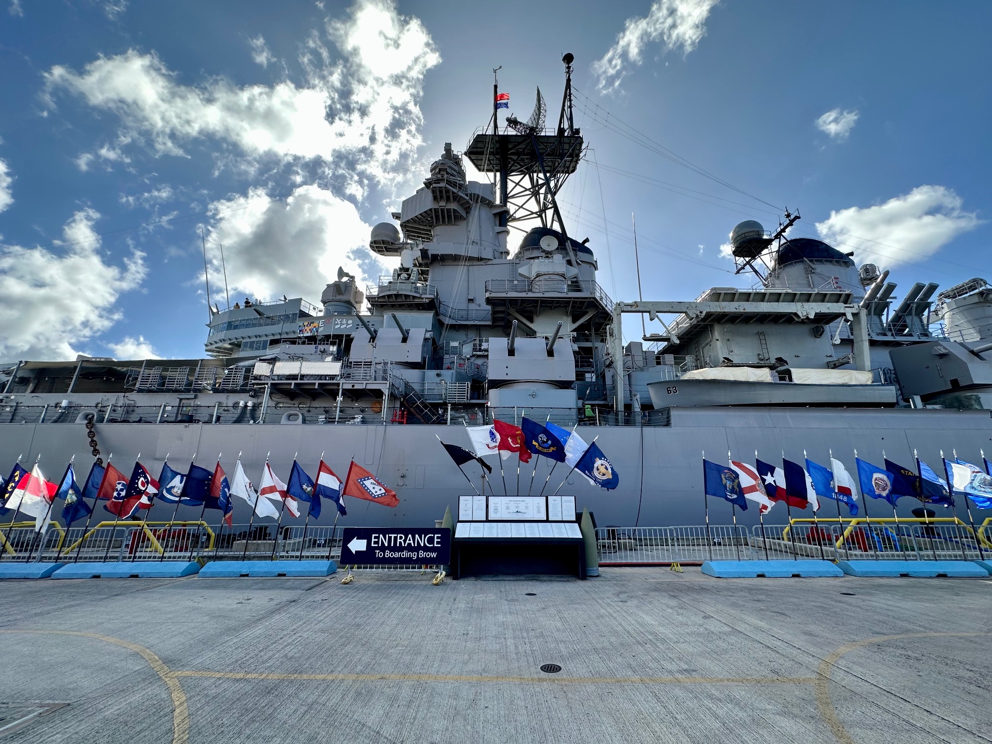 A white naval military ship with multiple flags displayed at its bow, docked at a Hawaiian port