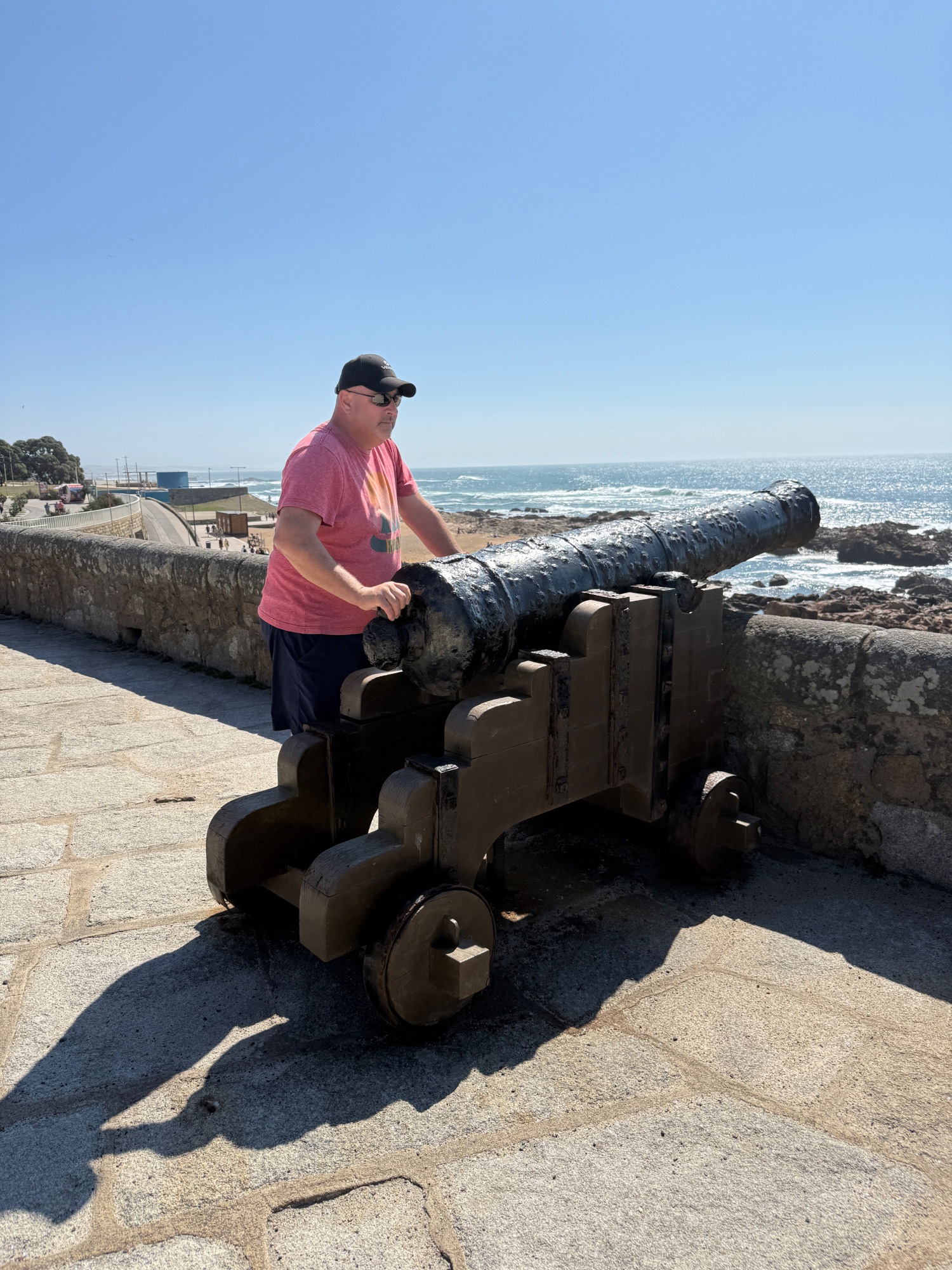 Man in pink shirt standing beside an old cannon overlooking the Atlantic Ocean and rocky coastline