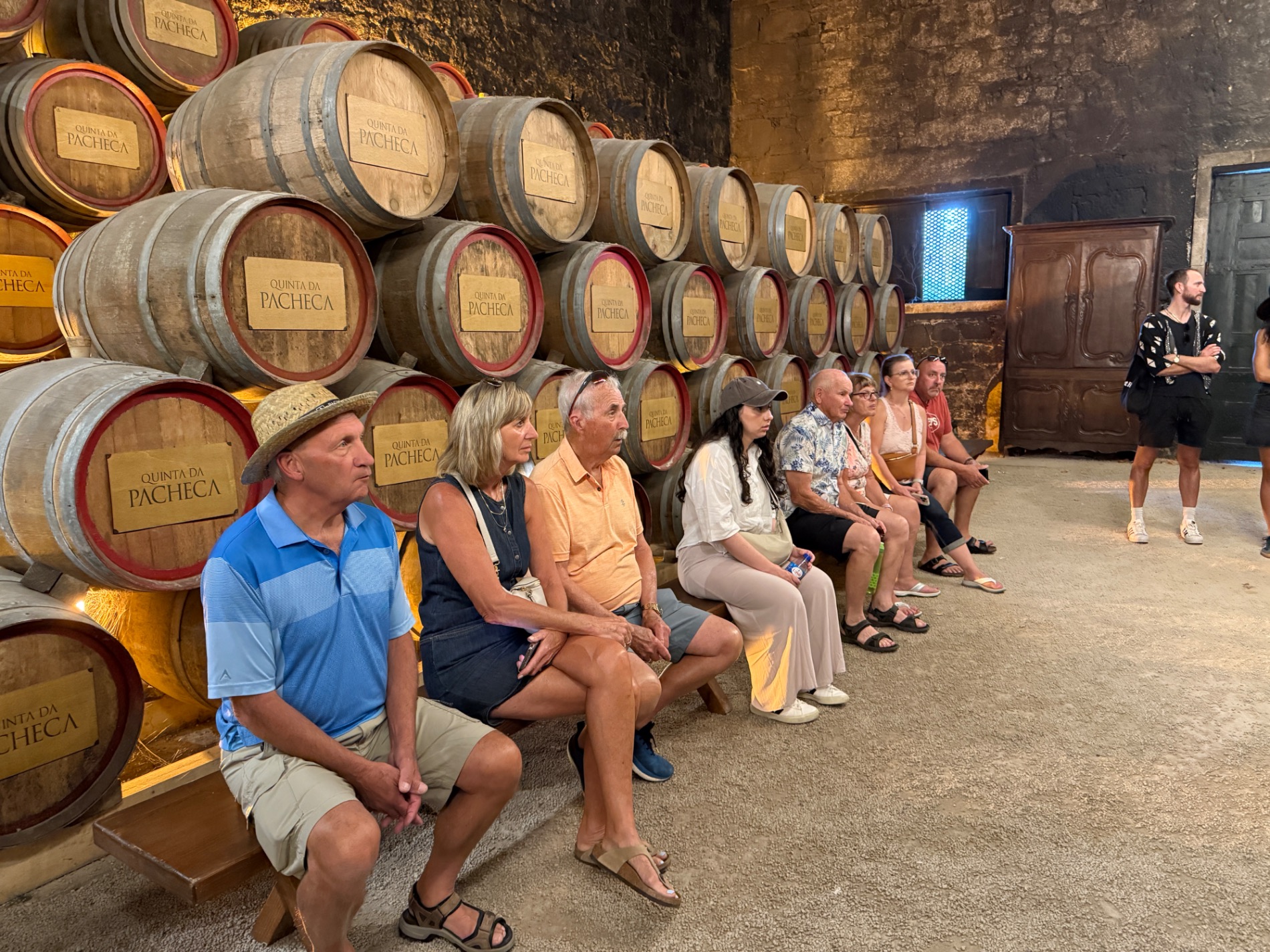 Visitors seated in front of large wooden wine barrels labeled Quinta da Pacheca in a cellar