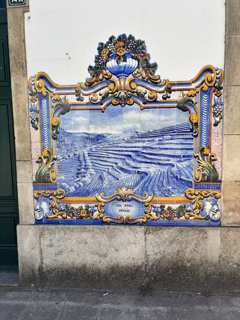 Ornate blue and white azulejo tile panel depicting vineyard landscape, mounted on a white building wall