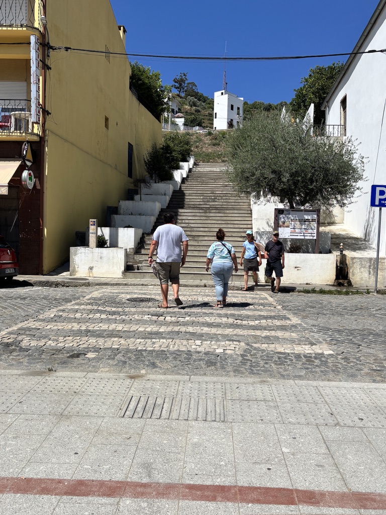 Pedestrians climbing a wide stone staircase in a hillside village with white and yellow buildings