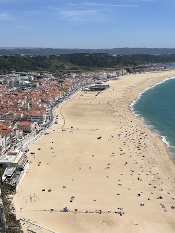 Aerial view of Nazaré beach with golden sand, turquoise water, and beachgoers scattered across the shore