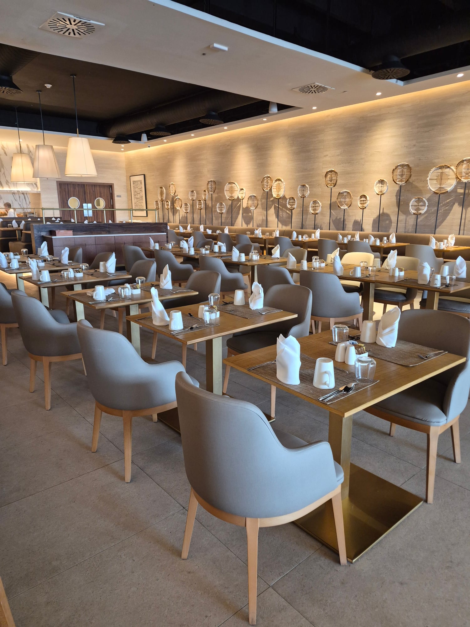 Modern restaurant dining room with gray upholstered chairs, wooden tables, and decorative badminton rackets on beige wall