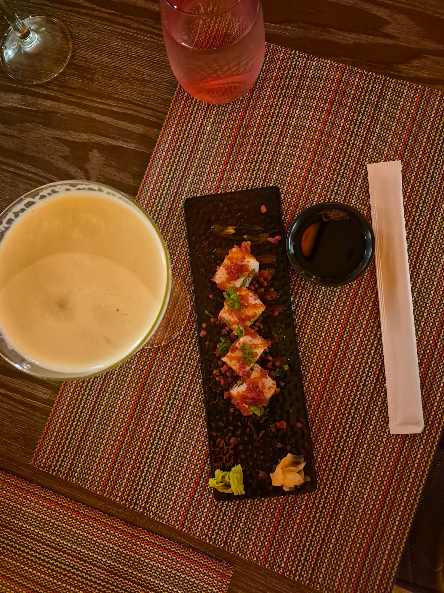 Overhead shot of appetizer plate with soup, sushi rolls, and sauce on a textured placemat