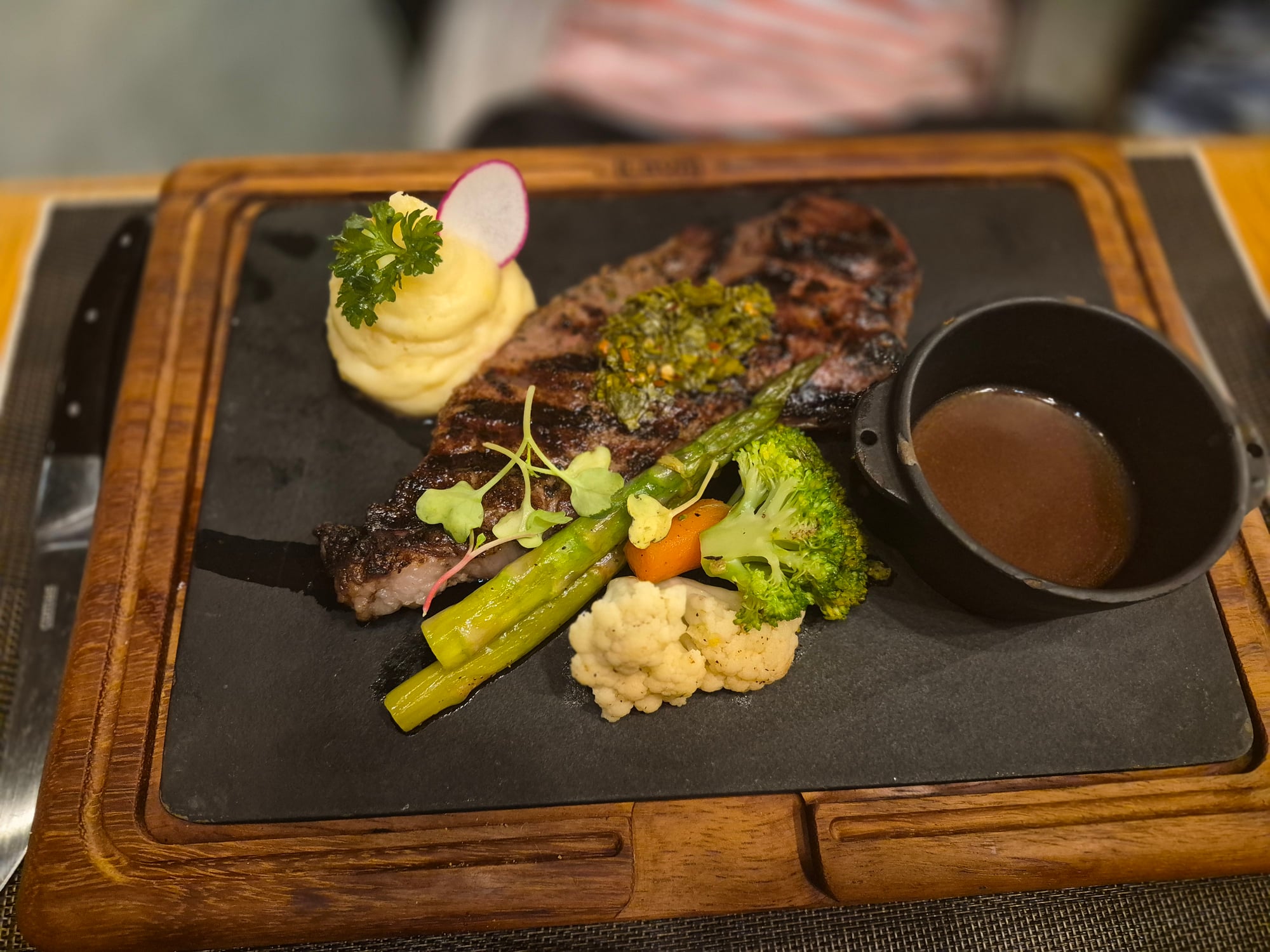 Plated steak with roasted vegetables, mashed potatoes, and sauce on black slate