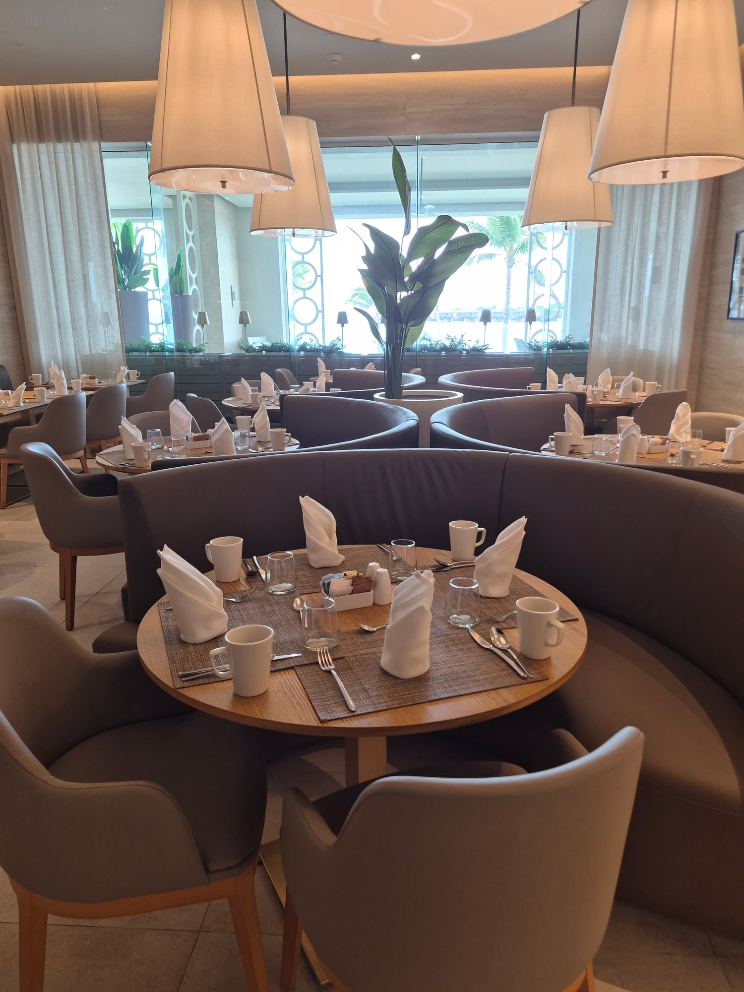 Modern dining room with curved banquettes, round tables, pendant lighting, and ocean views through windows