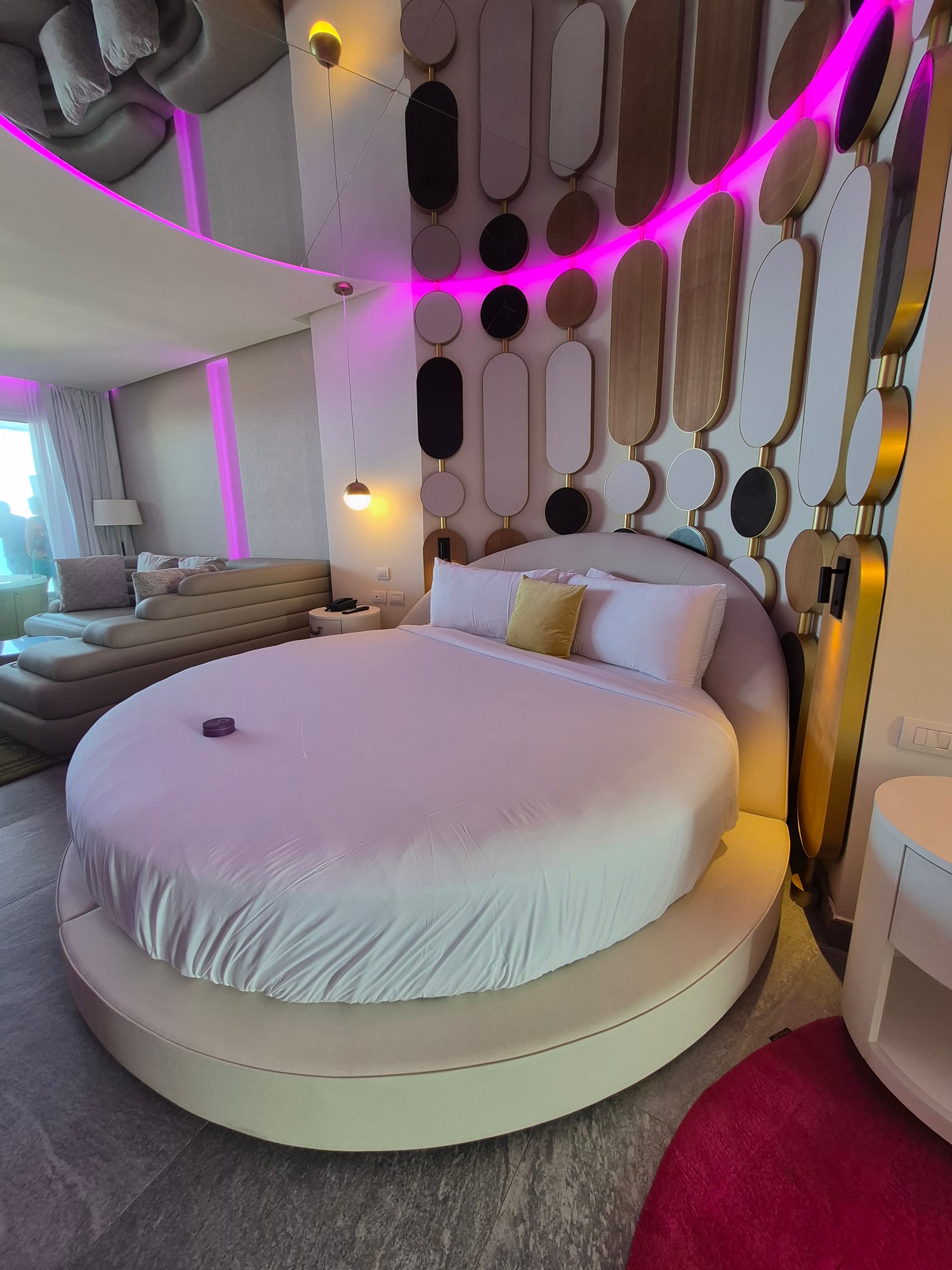 Elegant lounge area with curved cream sofa, decorative screens, and colorful pendant chandelier