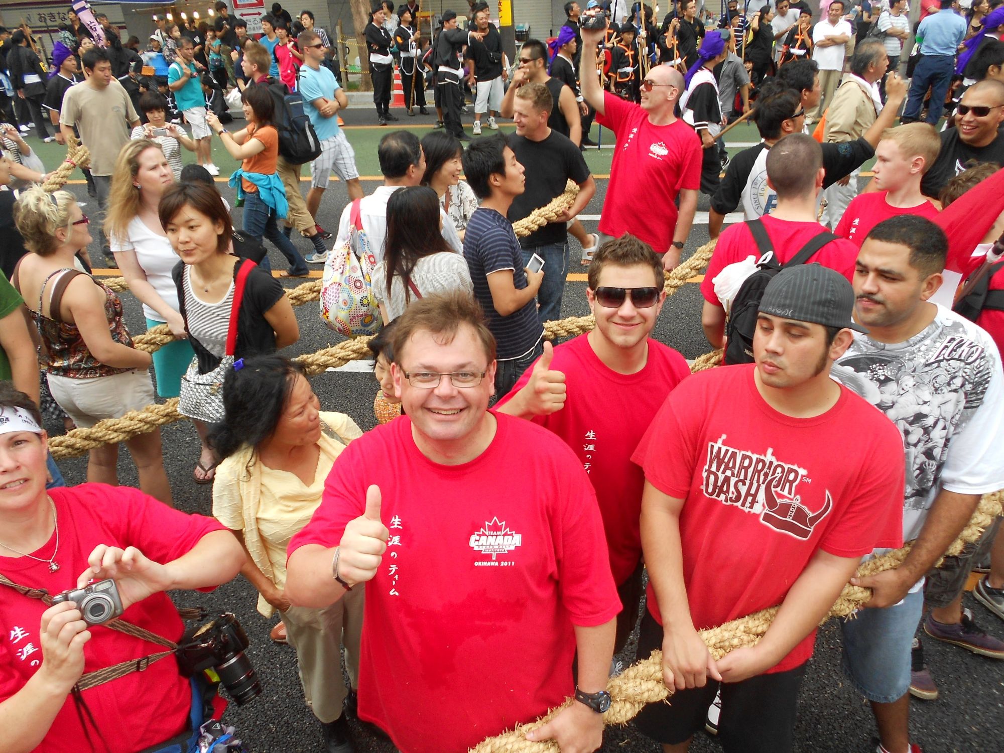 Large crowd of people in red shirts pulling a massive thick rope during a tug-of-war festival event
