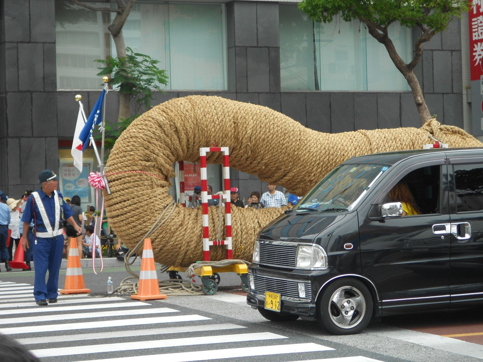 Another view of the giant rope sculpture with a vehicle and official in traditional dress nearby