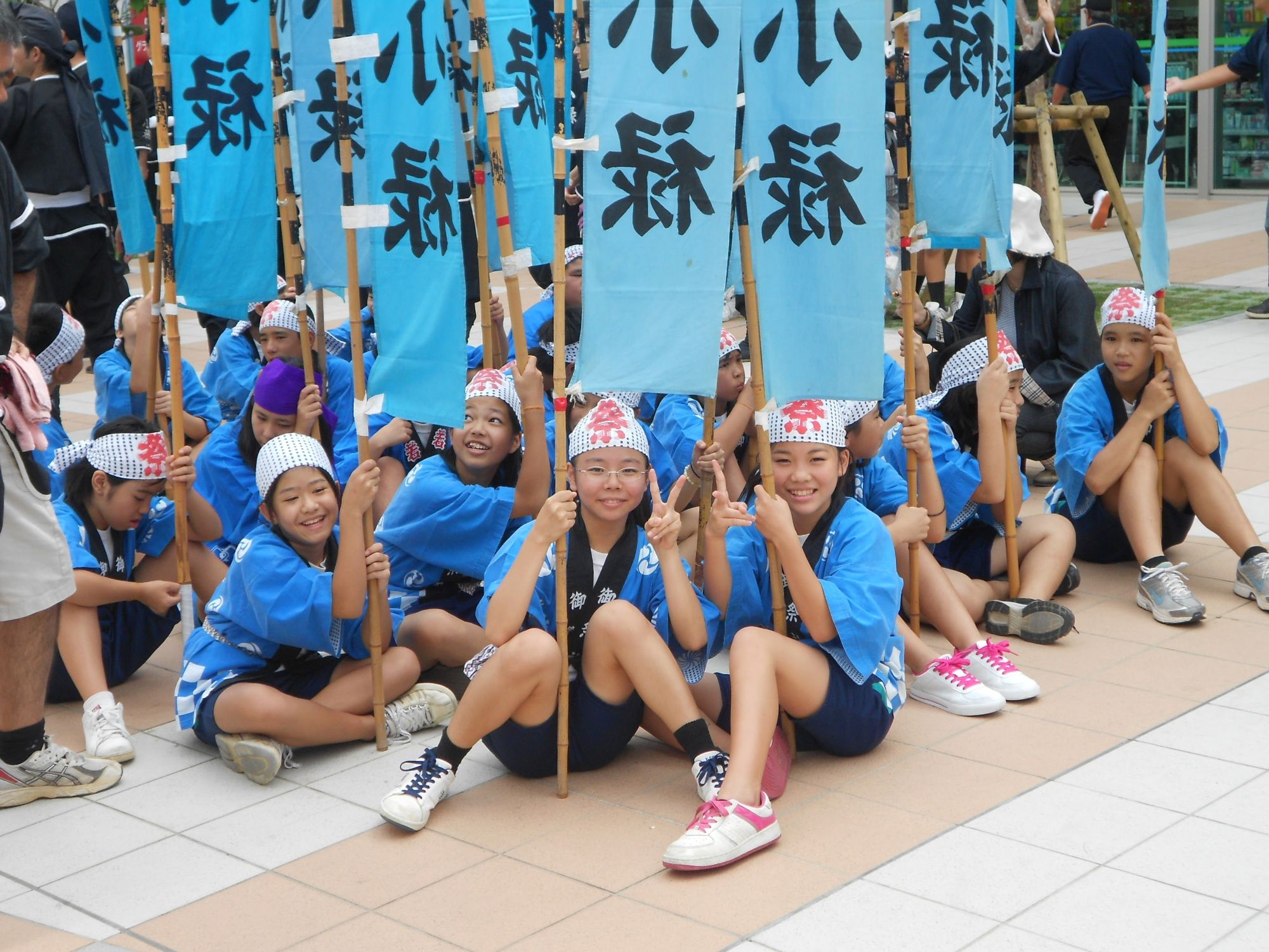 Young girls in blue festival clothing and headbands holding flags with Japanese characters