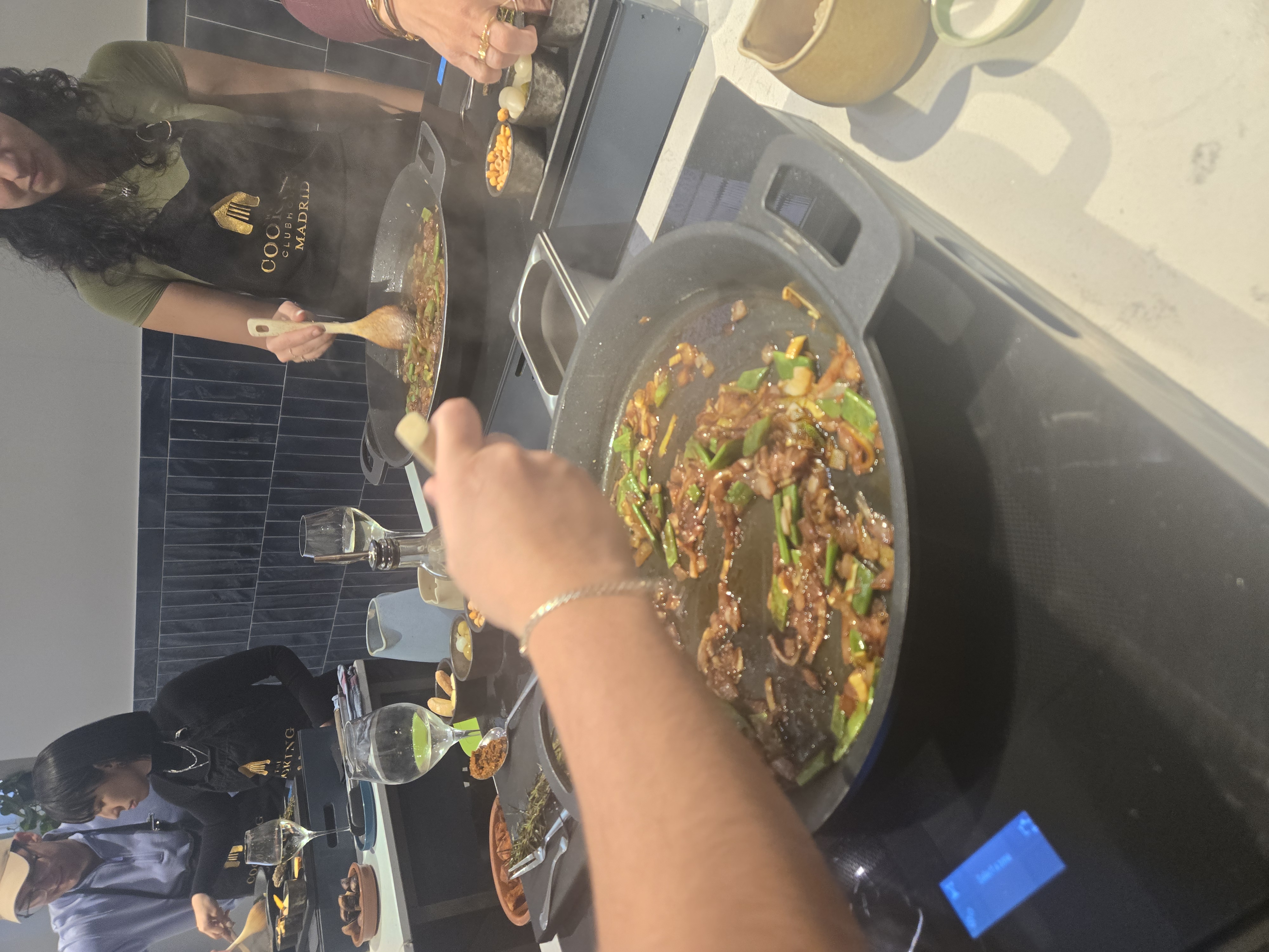 Hands stir a large pan of paella with green onions and meat at a Madrid cooking class