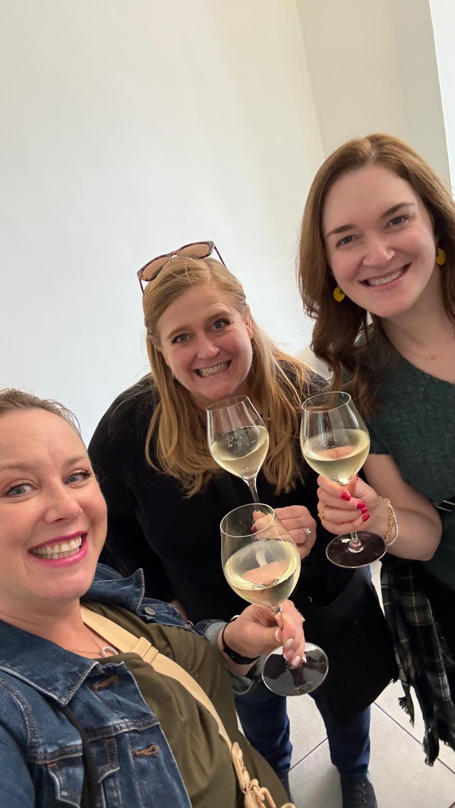 Three women hold glasses of white wine and smile at a Spanish wine tasting event