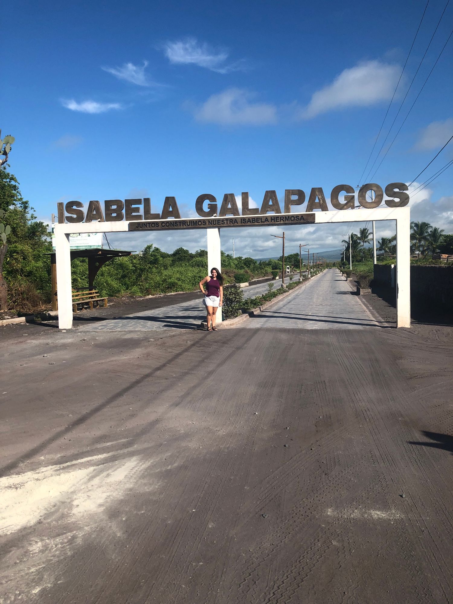 Beth Sharry standing under the Isabela Galápagos welcome sign on a volcanic rock road