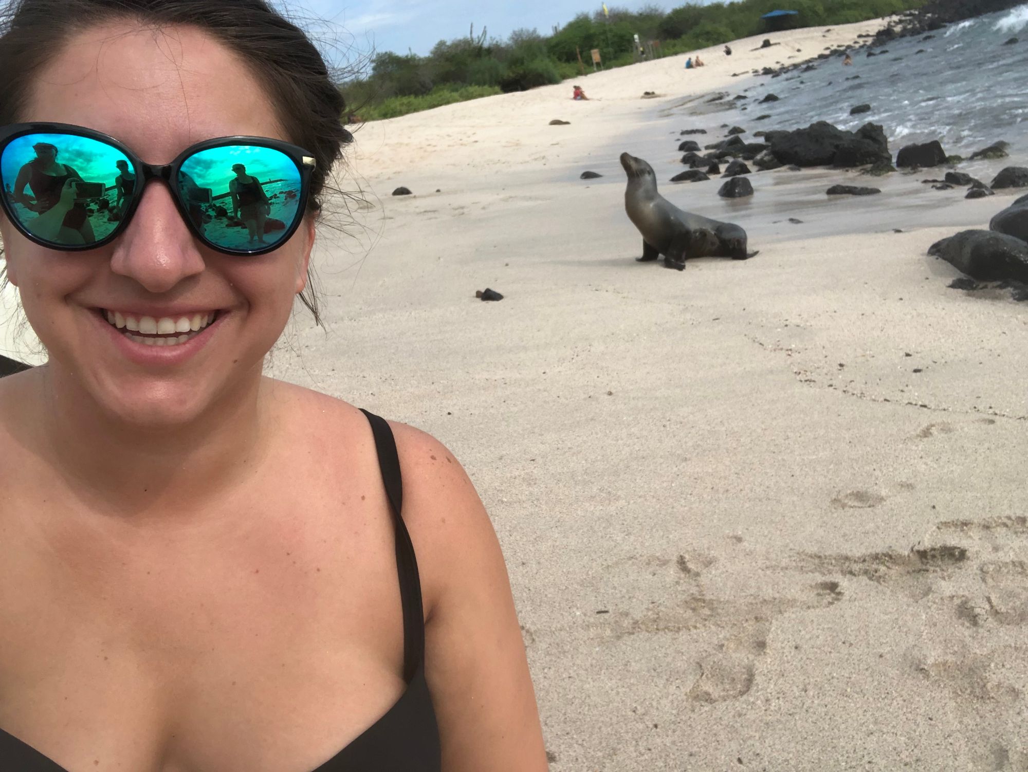 Beth Sharry on a white sand beach with Galápagos sea lions resting nearby