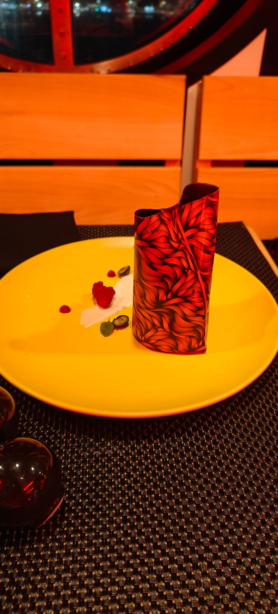 Red decorative cylindrical object on yellow plate with red heart shapes and small items on dark patterned surface
