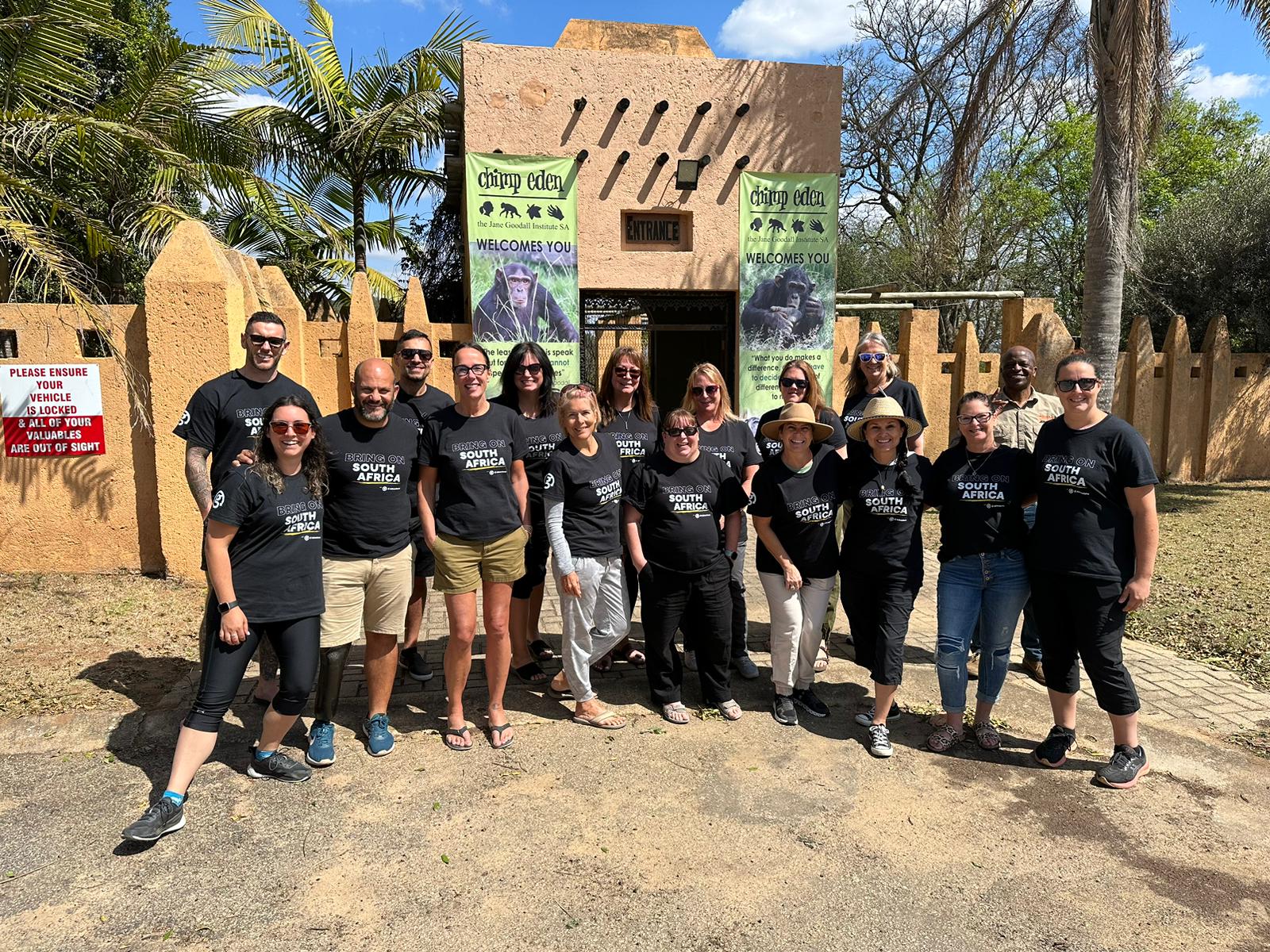 Group of tourists in matching black South Africa shirts stand outside Chimp Eden sanctuary entrance