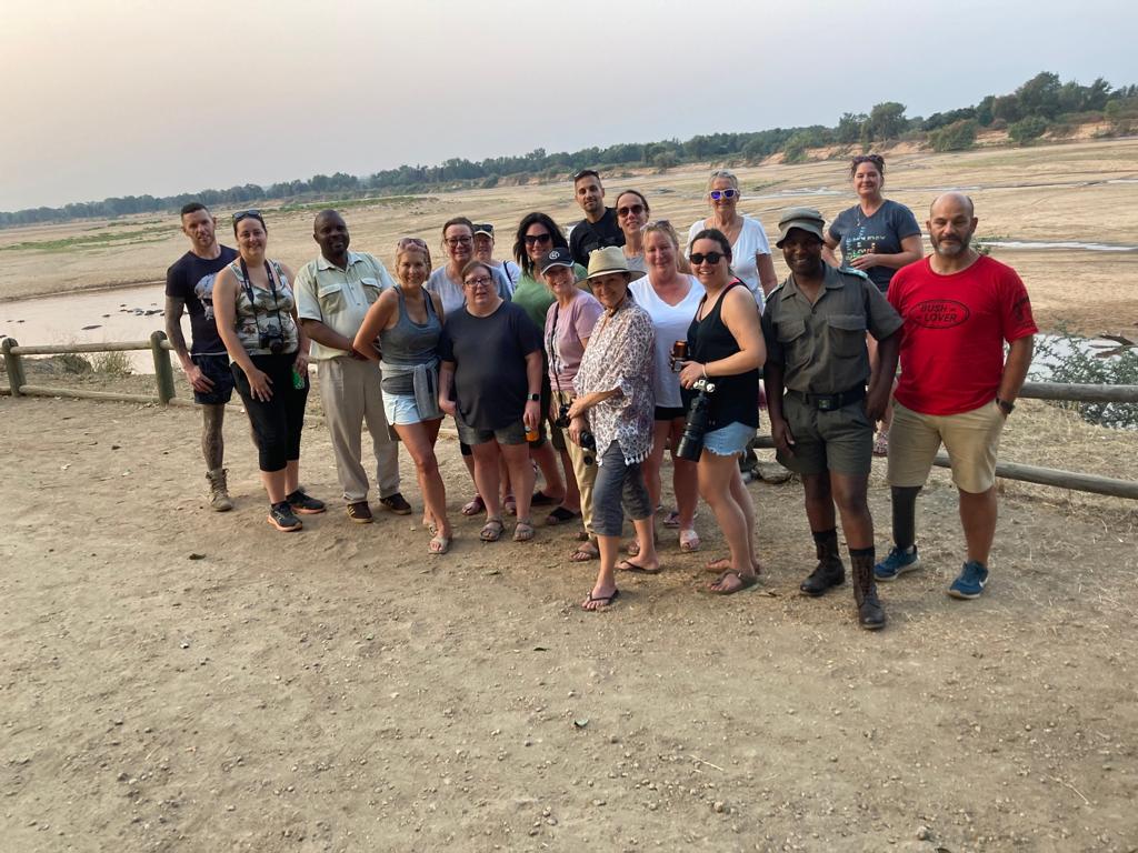 Group of tourists stand together on riverbank with wide landscape view in background