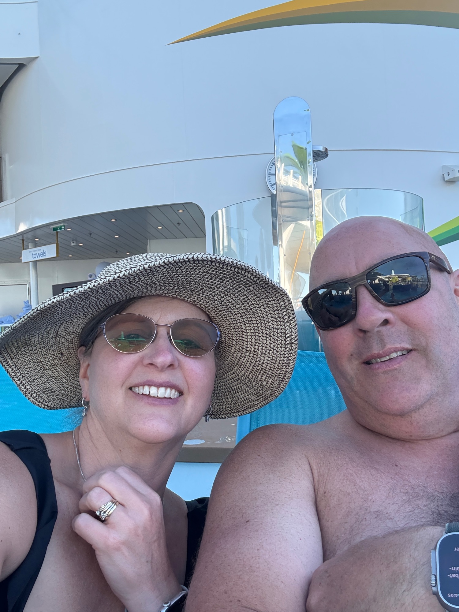 Woman in wide straw hat and sunglasses at a resort pool with colorful water slides in background