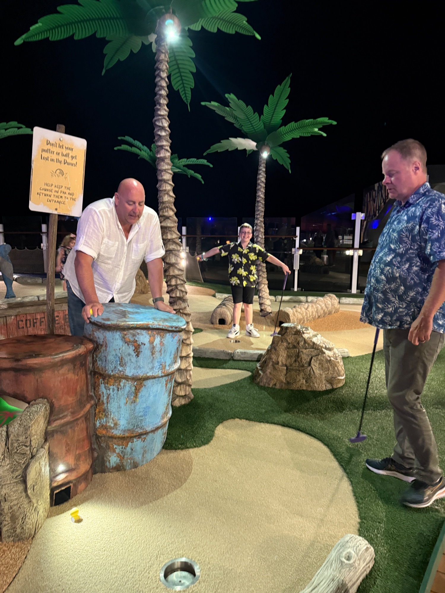 Person playing mini golf at night on a cruise ship with colorful course obstacles