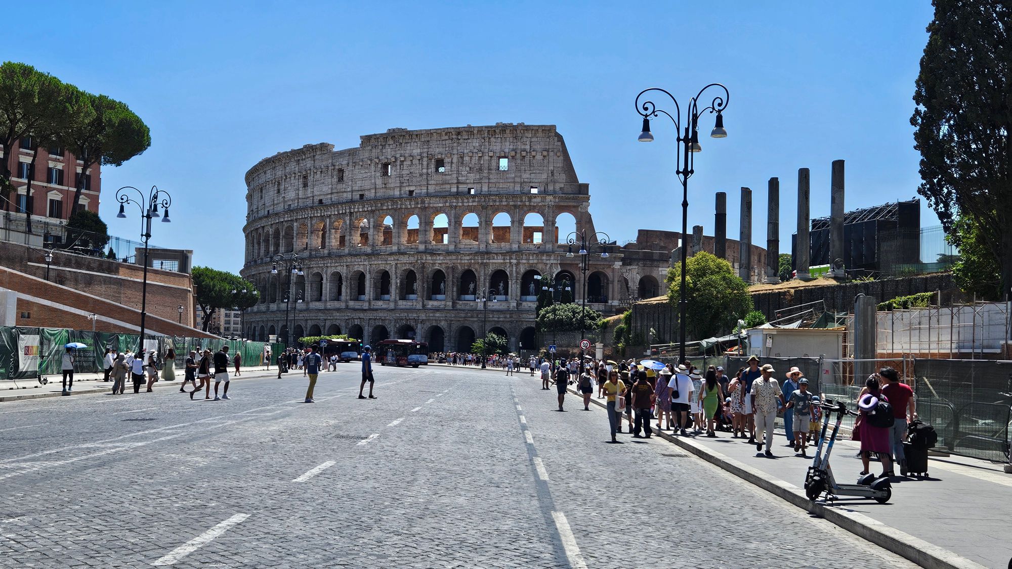 The Colosseum in Rome with tourists gathered in the plaza on a sunny day