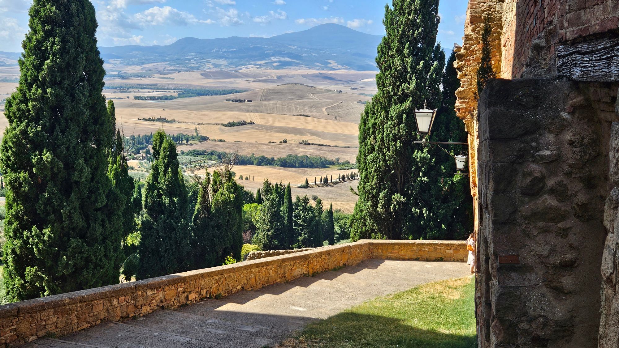 Tuscan countryside viewed through cypress trees lining a stone terrace with rolling hills beyond
