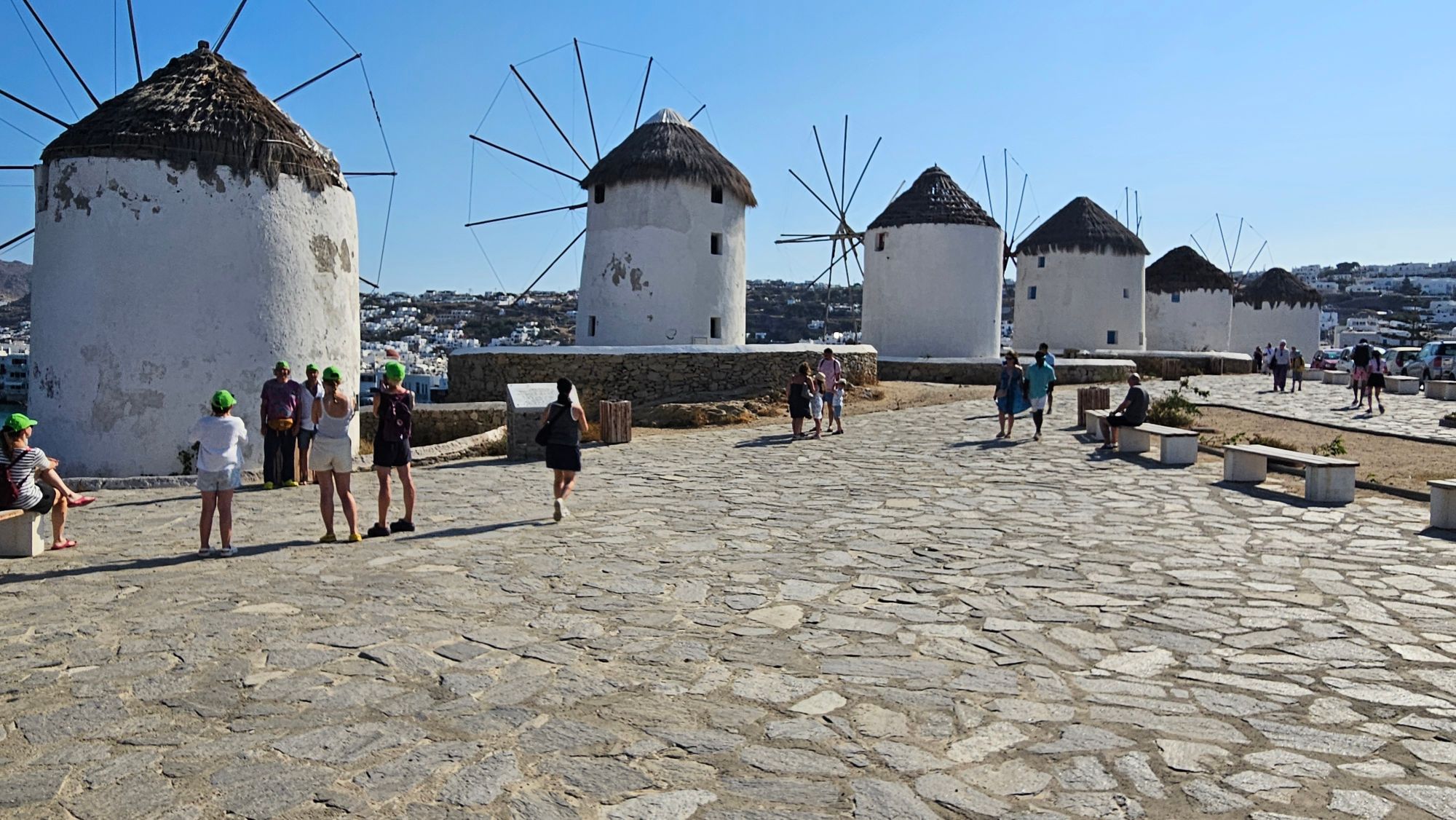 White windmills with thatched roofs on the island of Mykonos with the Aegean Sea and town behind