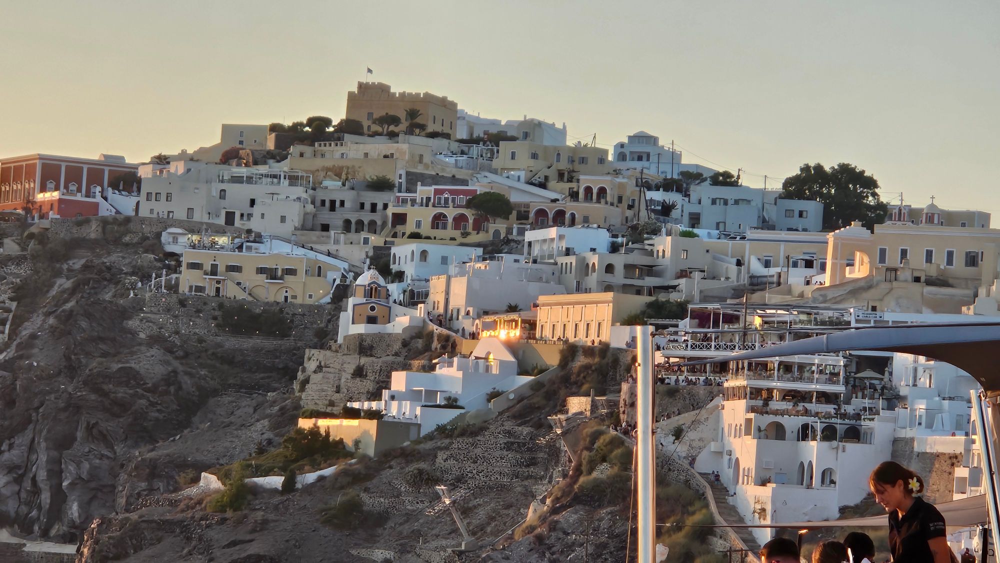 Sunset over Santorini's caldera with white architecture, blue domes, and cruise ships anchored below