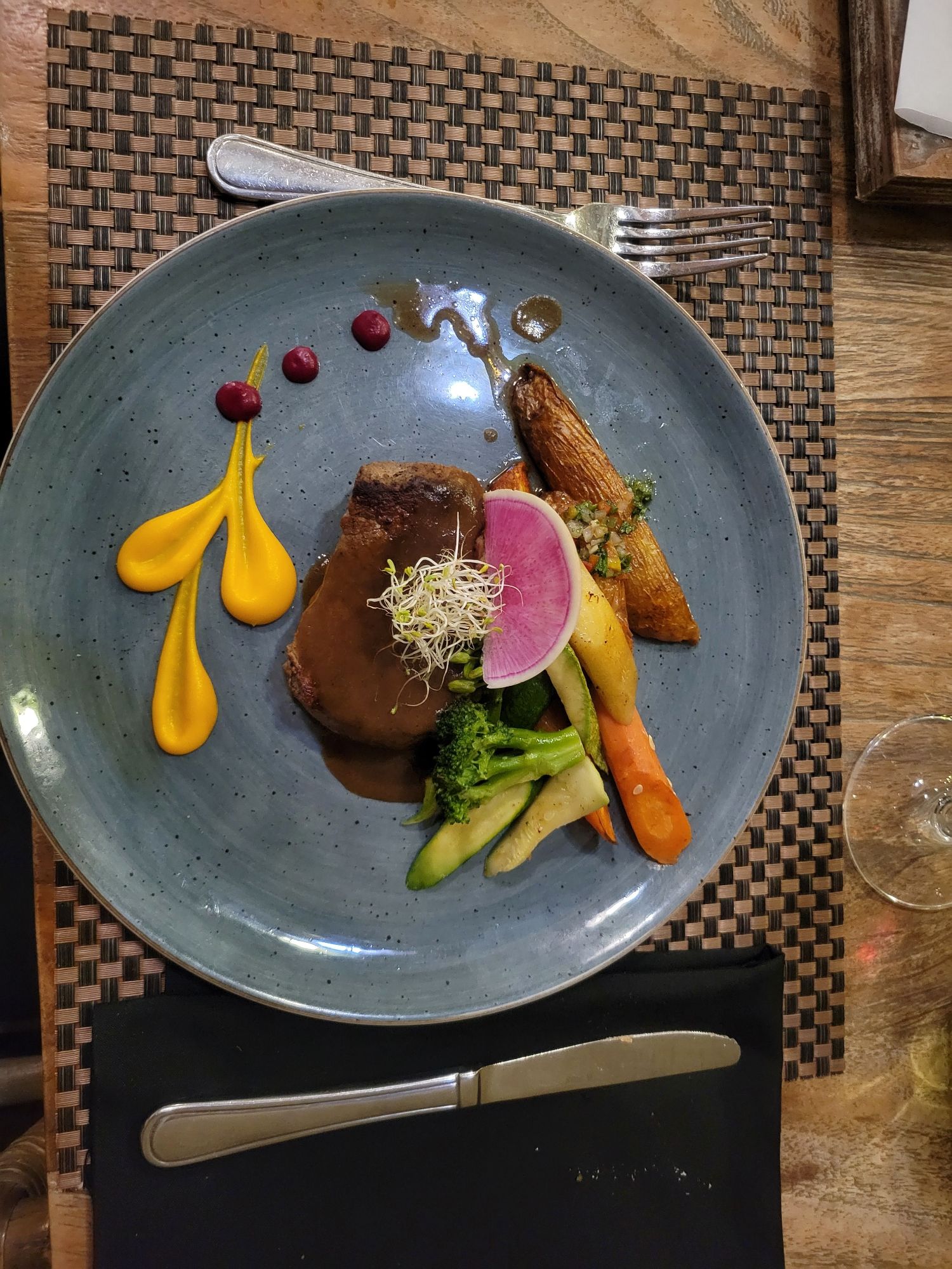 Artfully plated duck breast with vegetables and yellow sauce on a speckled blue plate at a fine dining restaurant